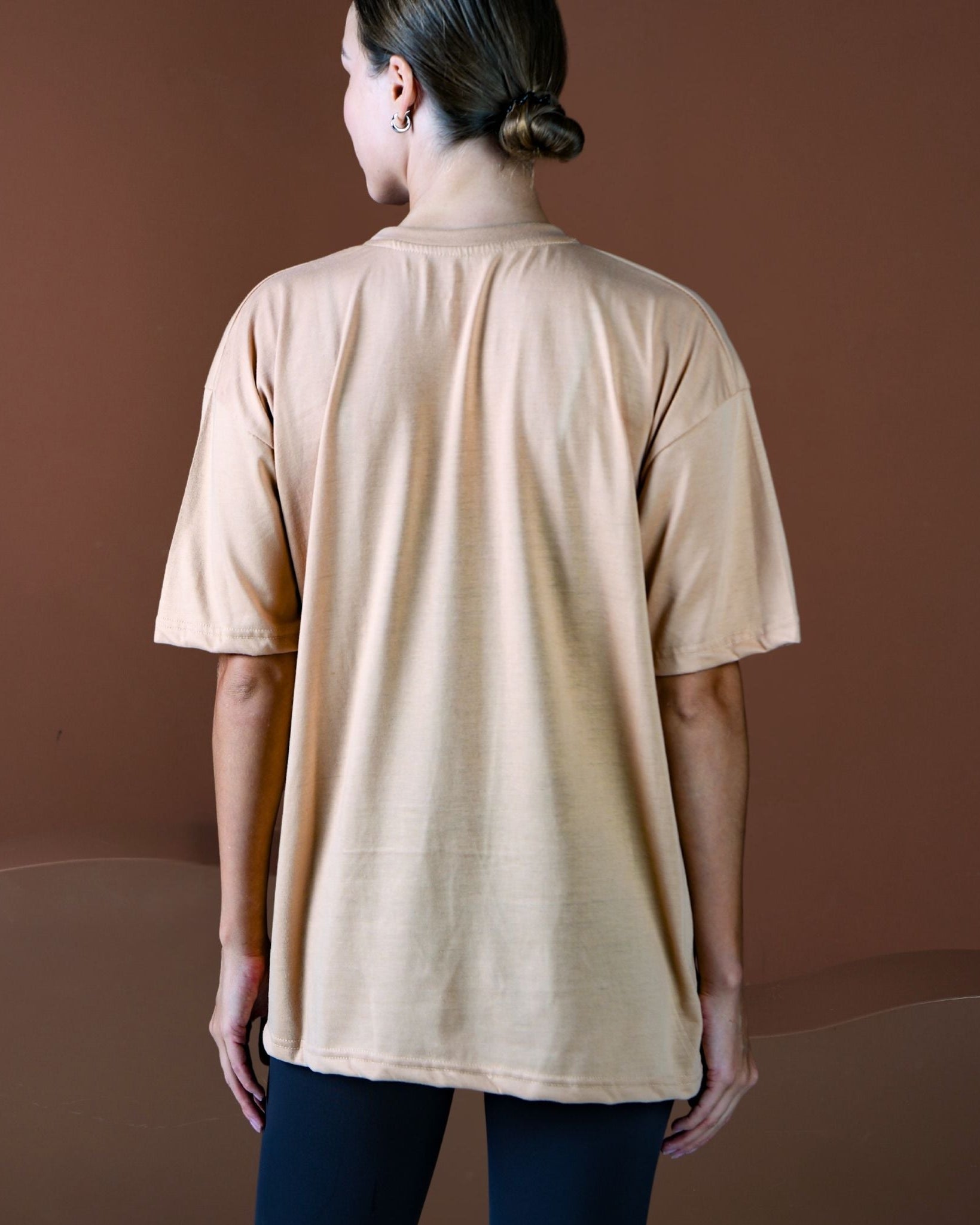 Person wearing a beige t-shirt against a brown background