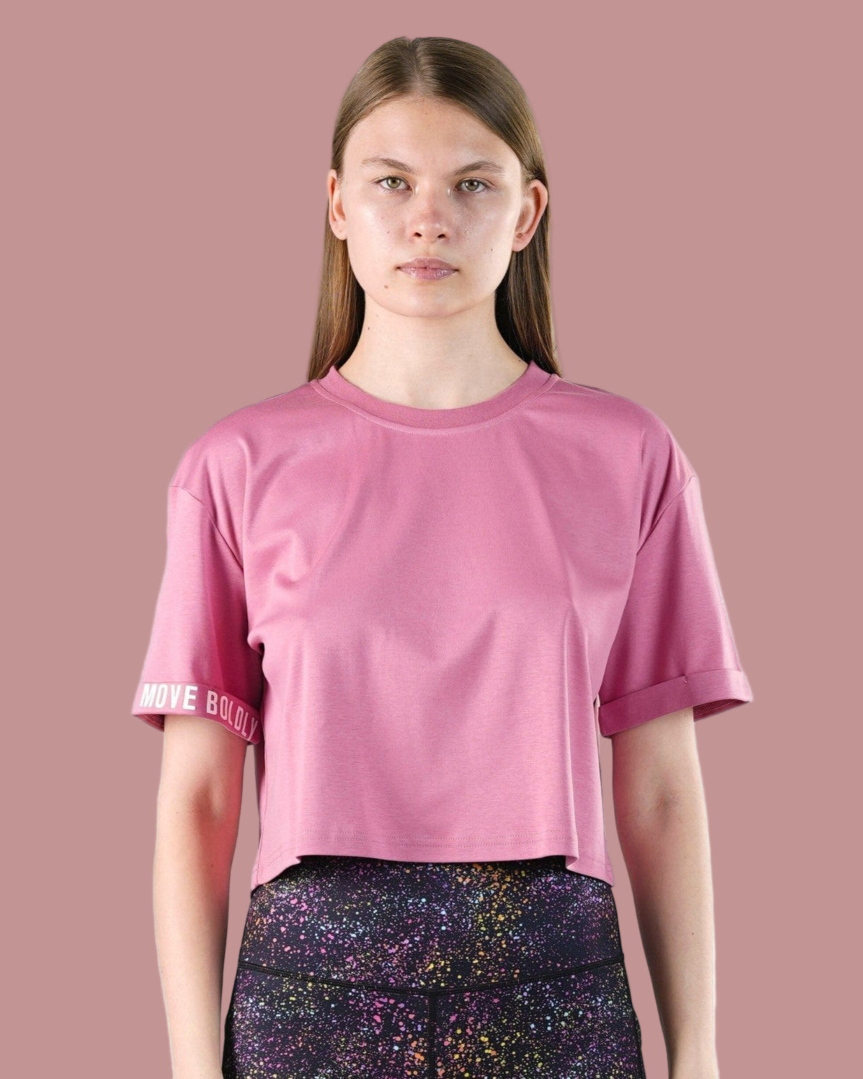 Person wearing a pink t-shirt with a brand logo on a pink background