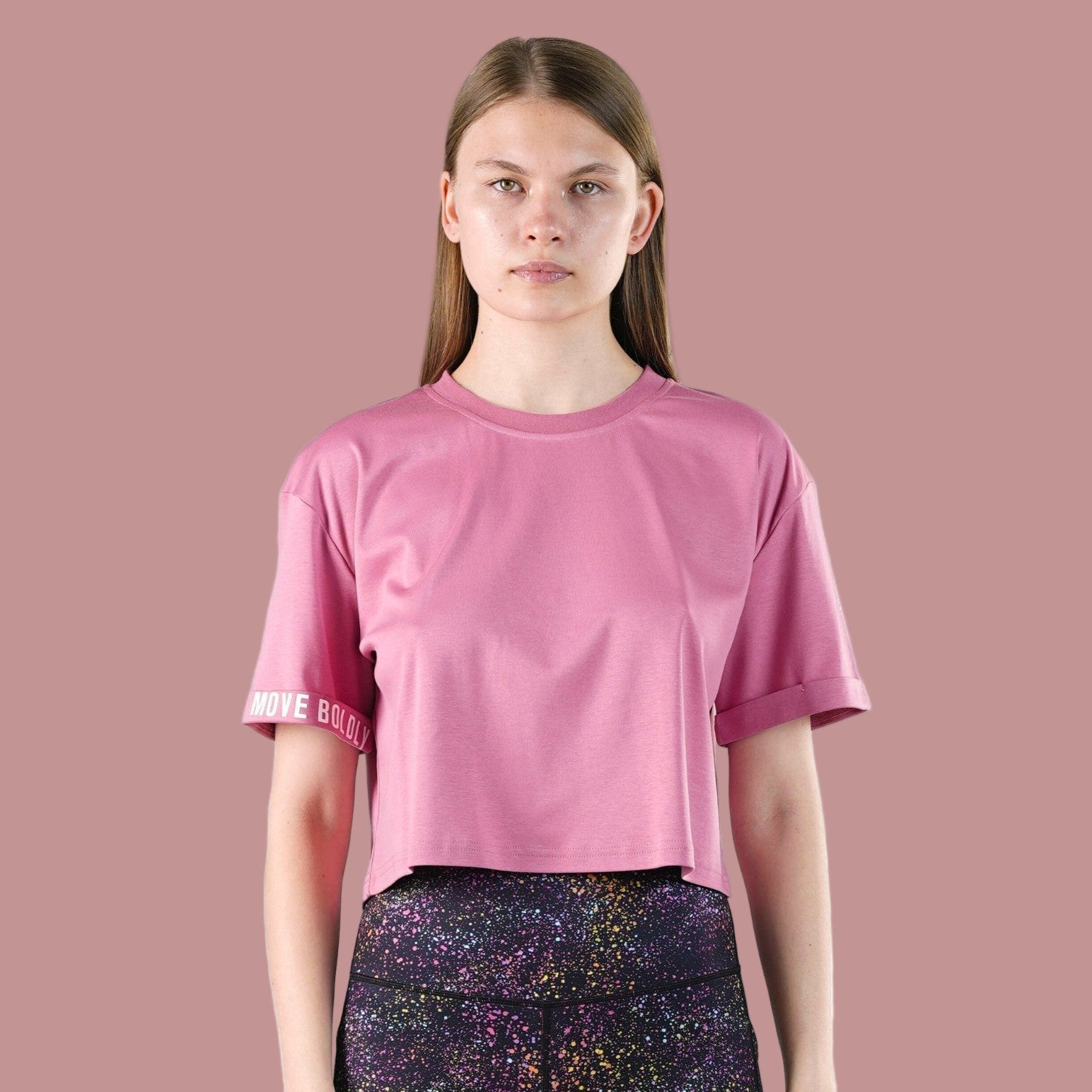 Person wearing a pink t-shirt with a brand logo on a pink background