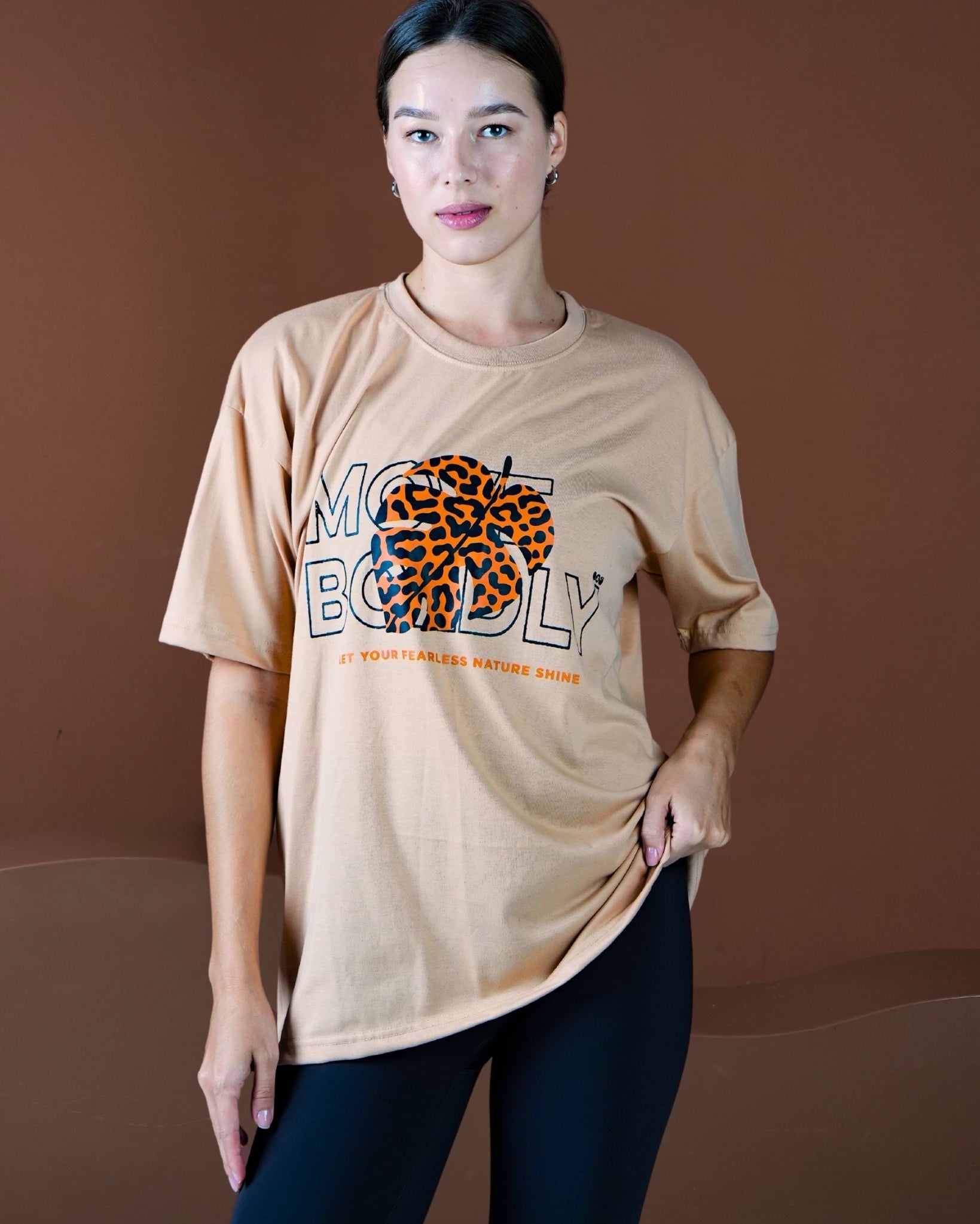 Woman wearing a beige t-shirt with a graphic design on a brown background