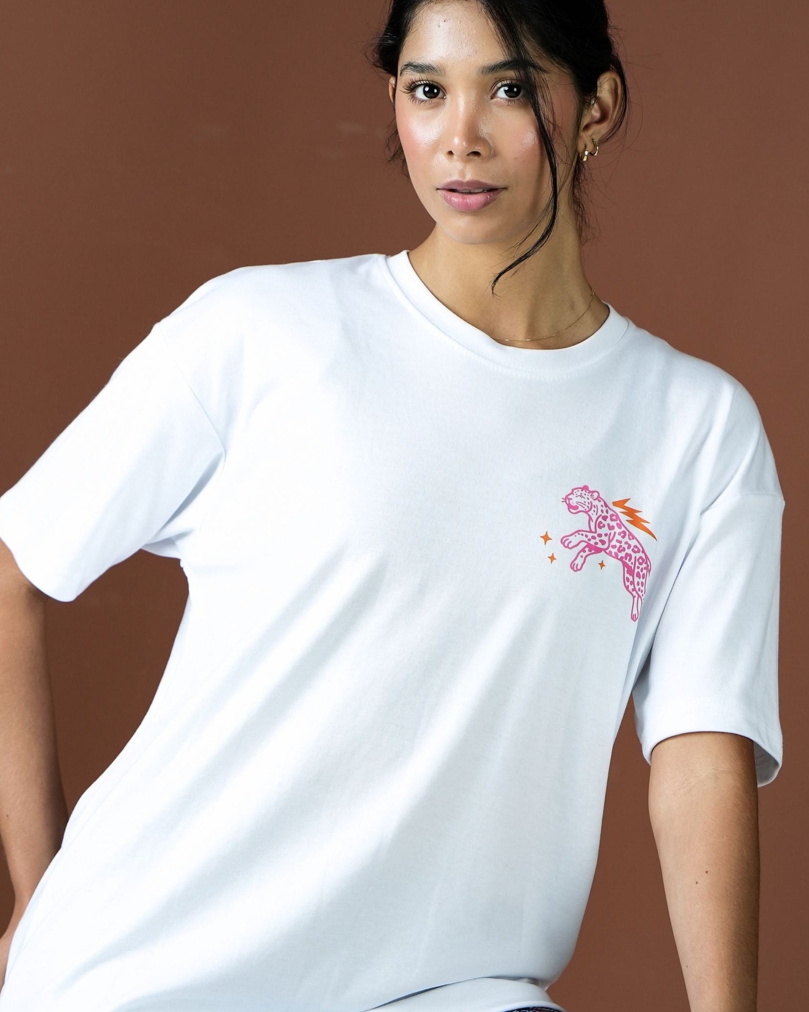 Woman wearing a white t-shirt with a pink and orange graphic on a brown background