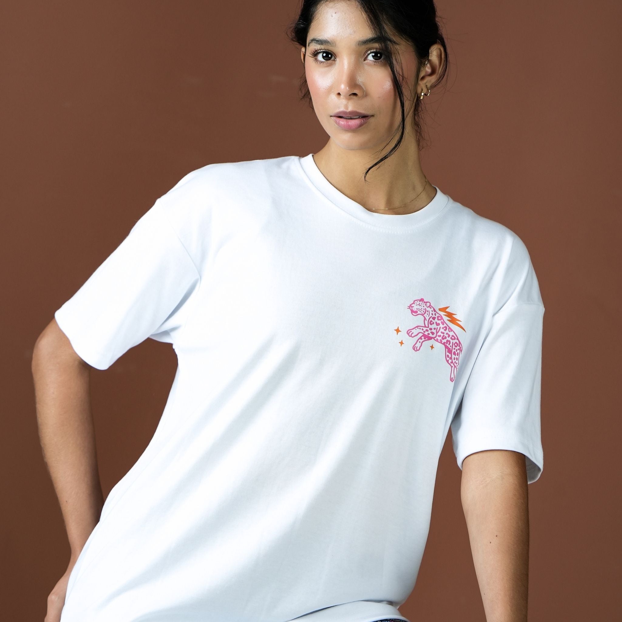 Woman wearing a white t-shirt with a pink and orange graphic on a brown background