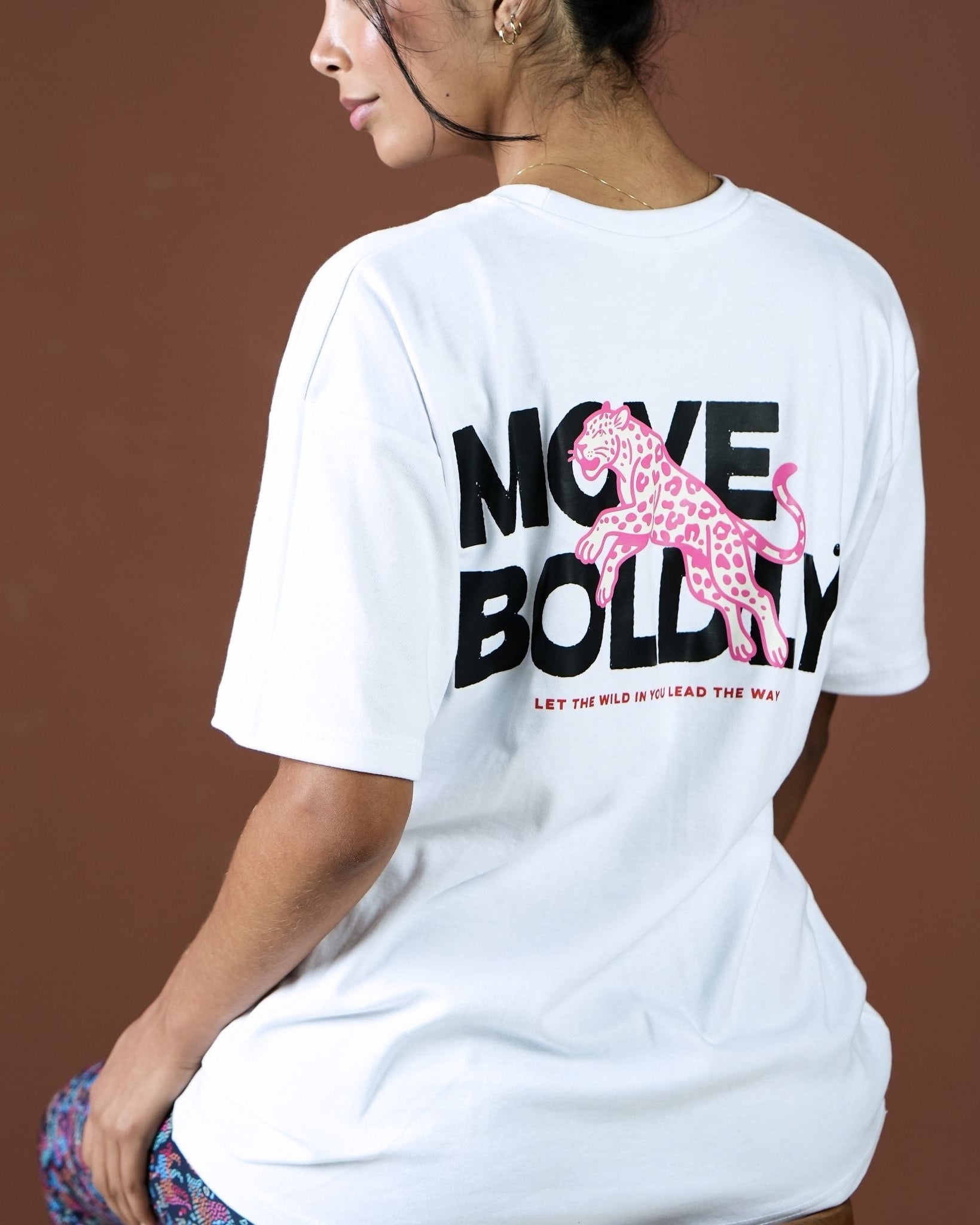 Person wearing a white t-shirt with a pink panther graphic and text on the back against a brown background