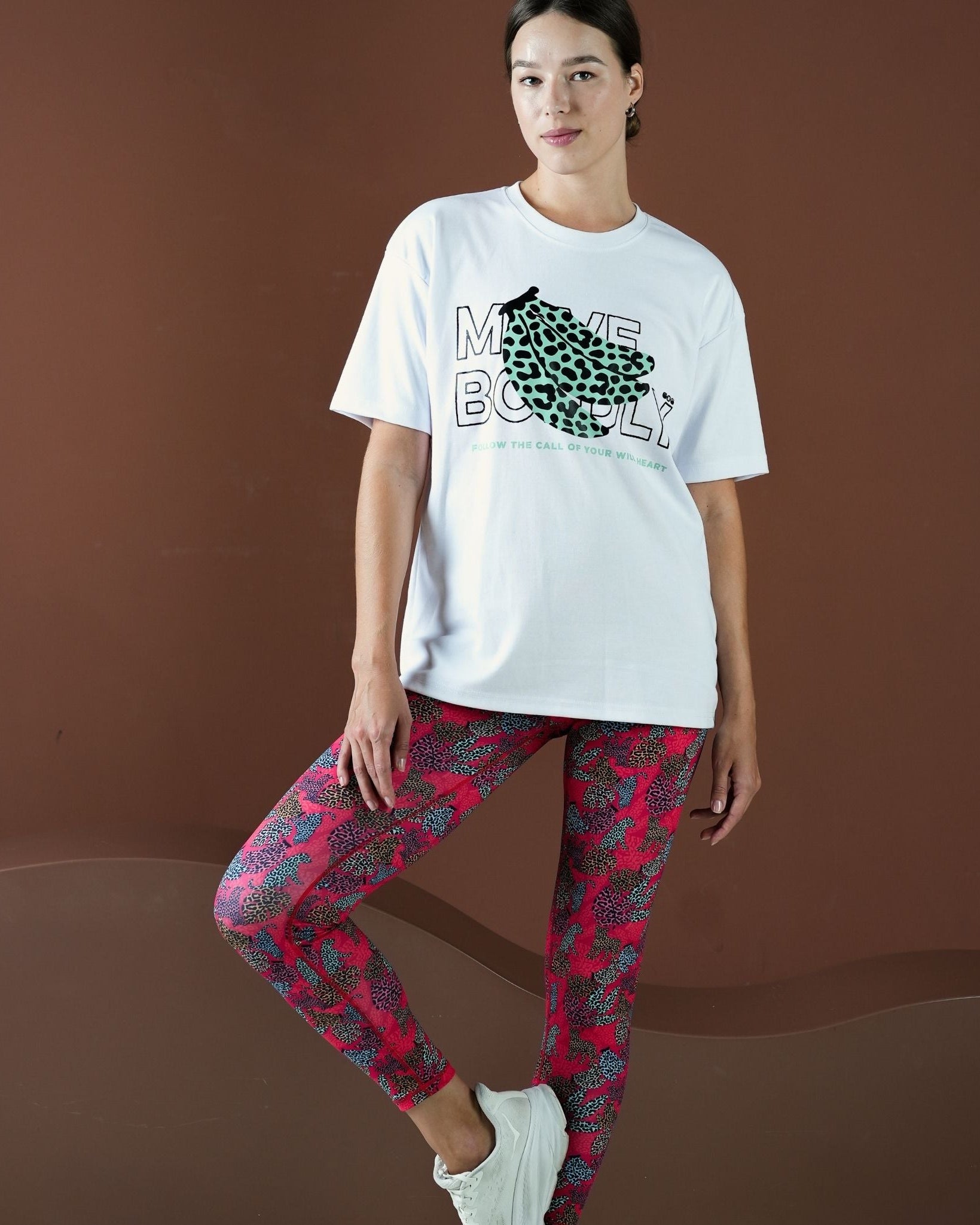 Person wearing a white t-shirt with a graphic design and red patterned leggings on a brown background
