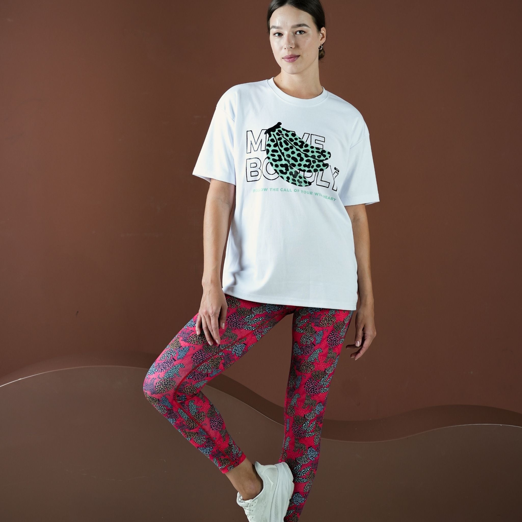 Person wearing a white t-shirt with a graphic design and red patterned leggings on a brown background
