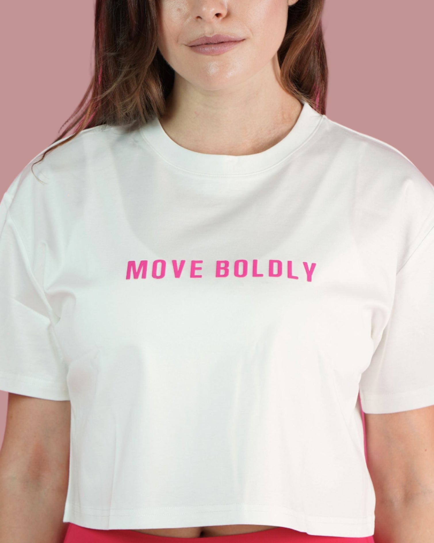 Person wearing a white crop top with 'MOVE BOLDLY' text on a pink background
