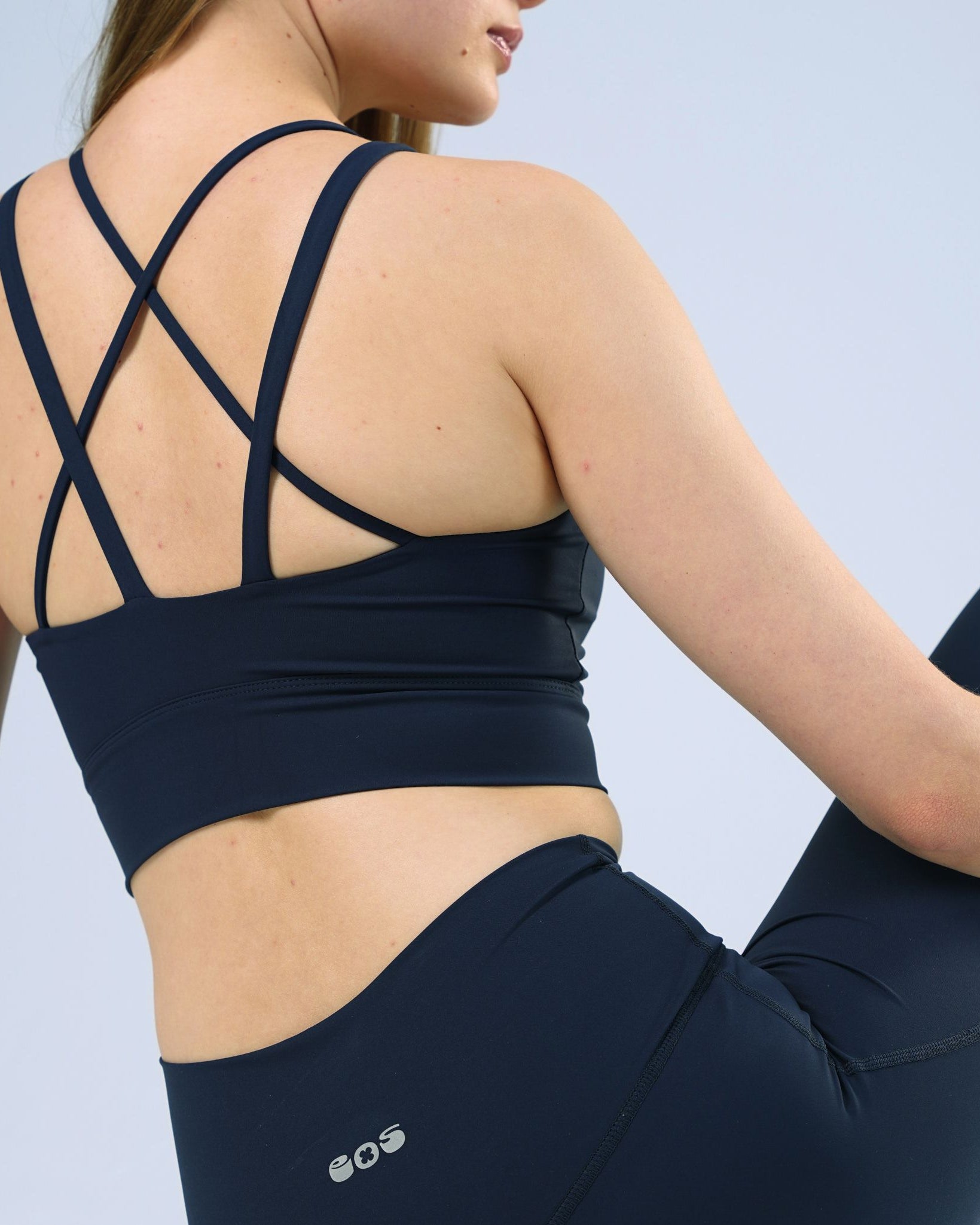 Person wearing a navy sports bra and leggings with a visible brand logo on a light blue background