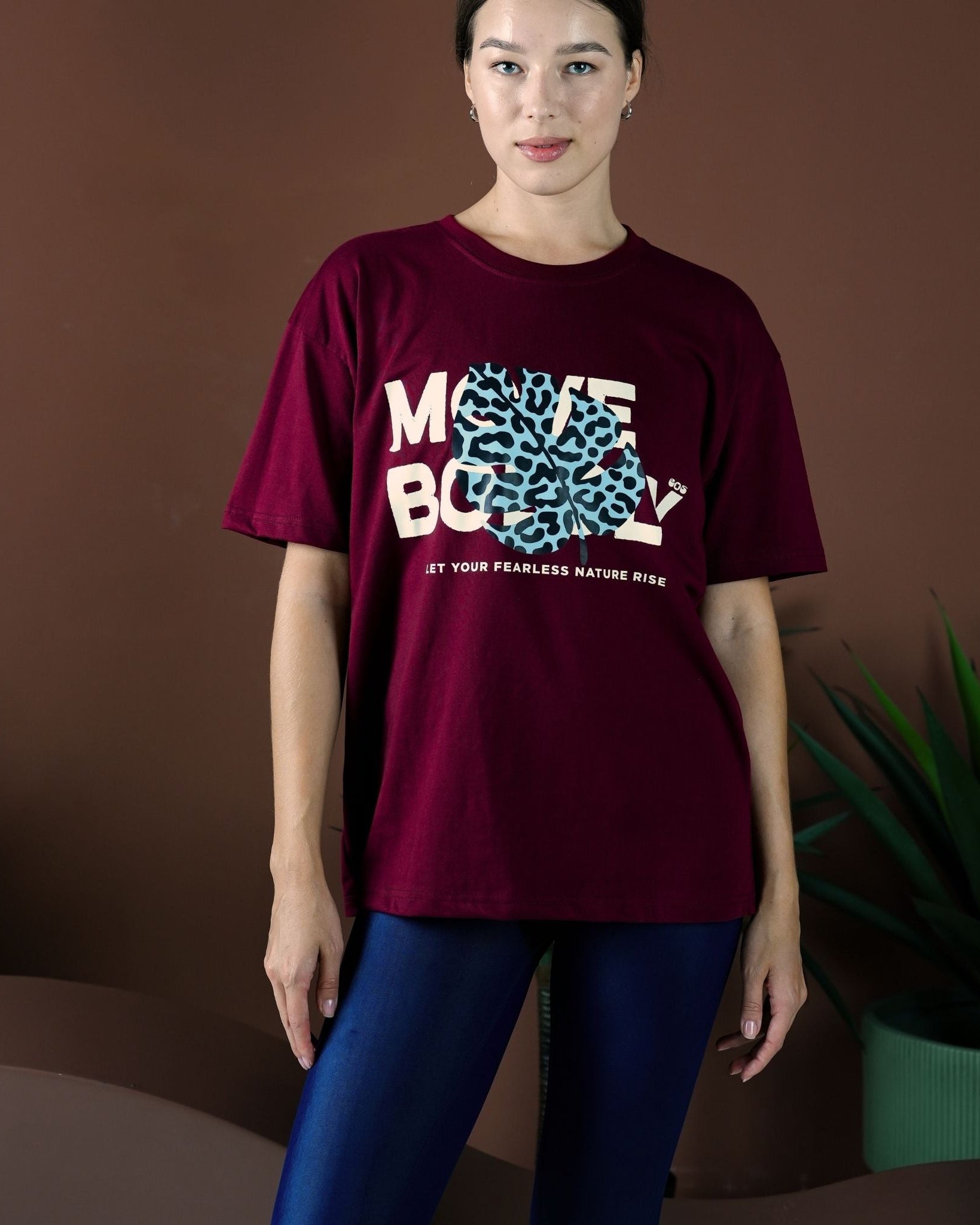 Person wearing a burgundy t-shirt with a graphic design on a brown background