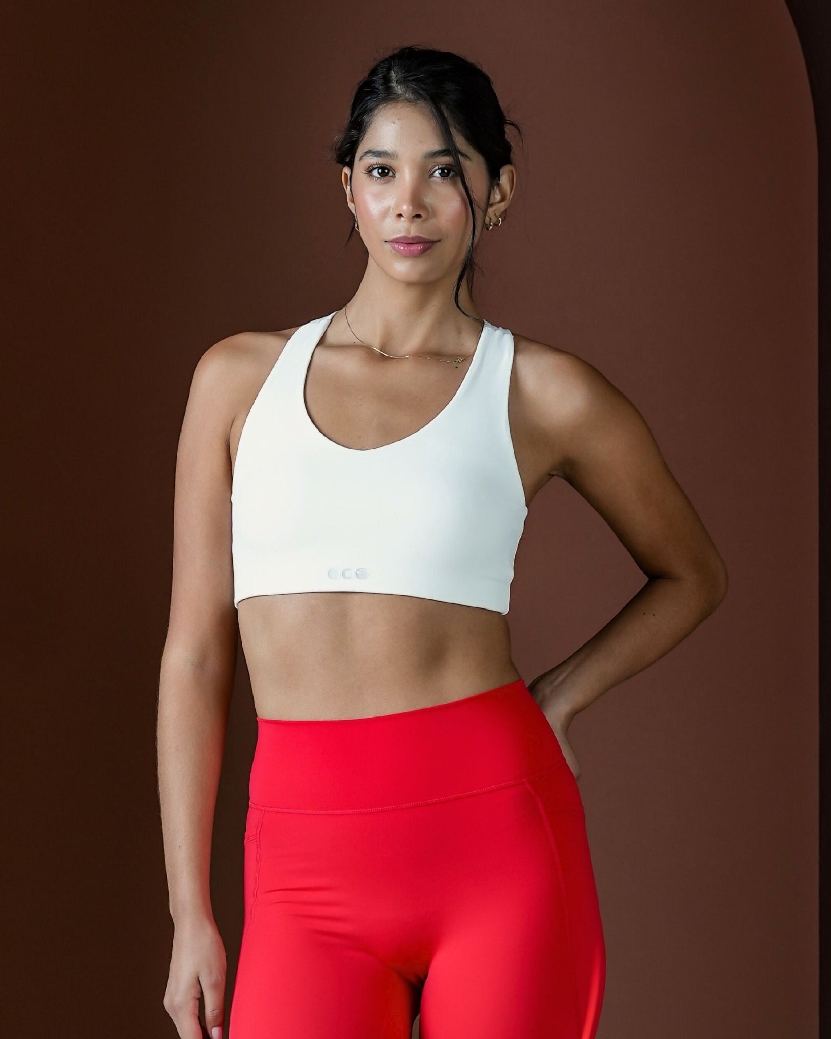 Woman wearing a white sports bra and red leggings against a brown background
