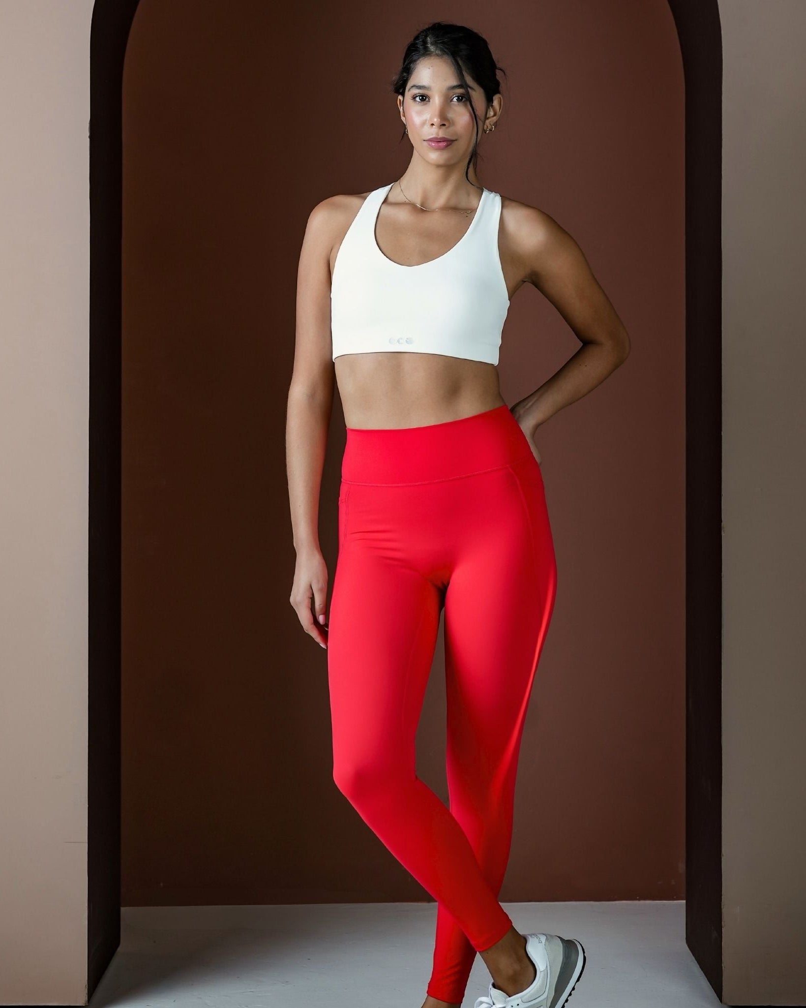 Woman wearing a white sports bra and red leggings against a brown background