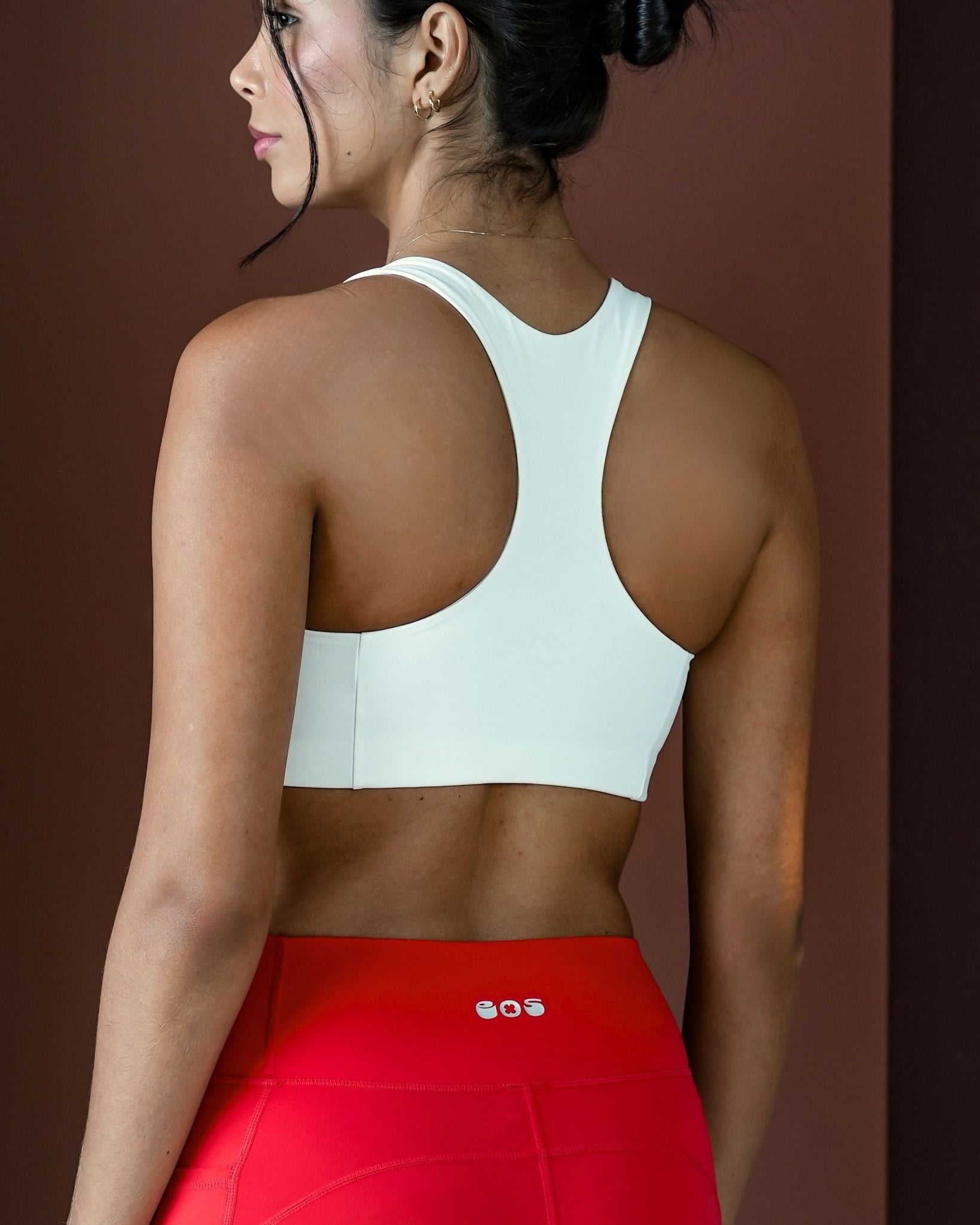 Woman wearing a white sports bra and red leggings against a brown background