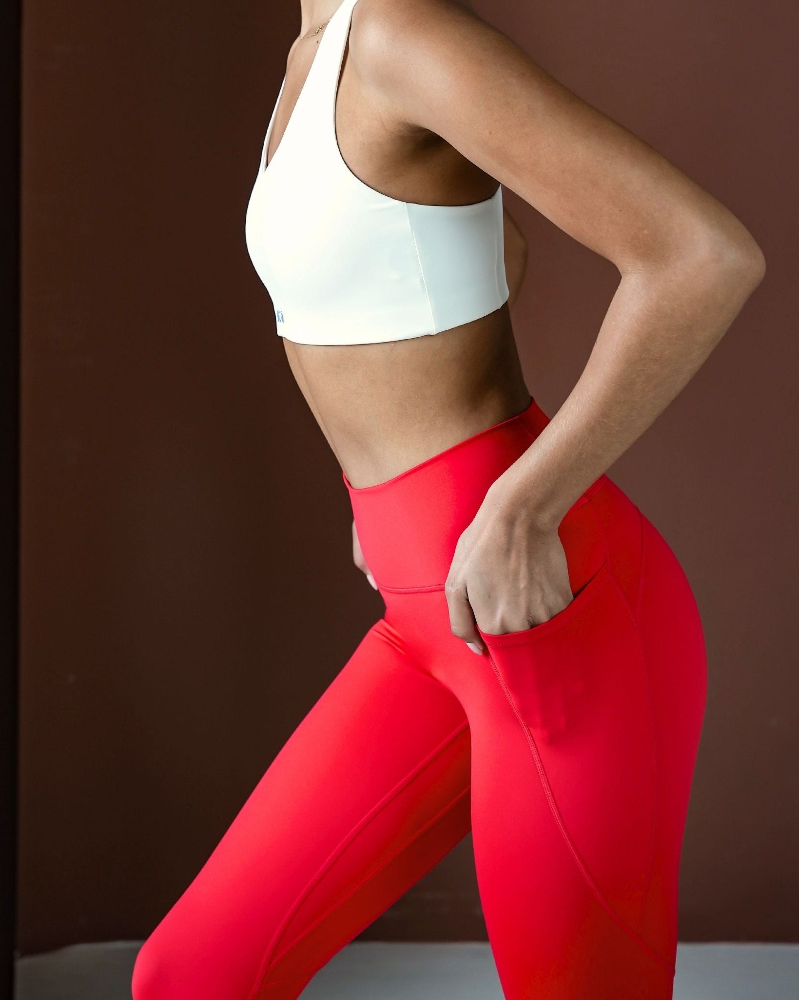 Person wearing a white sports bra and red leggings against a brown background