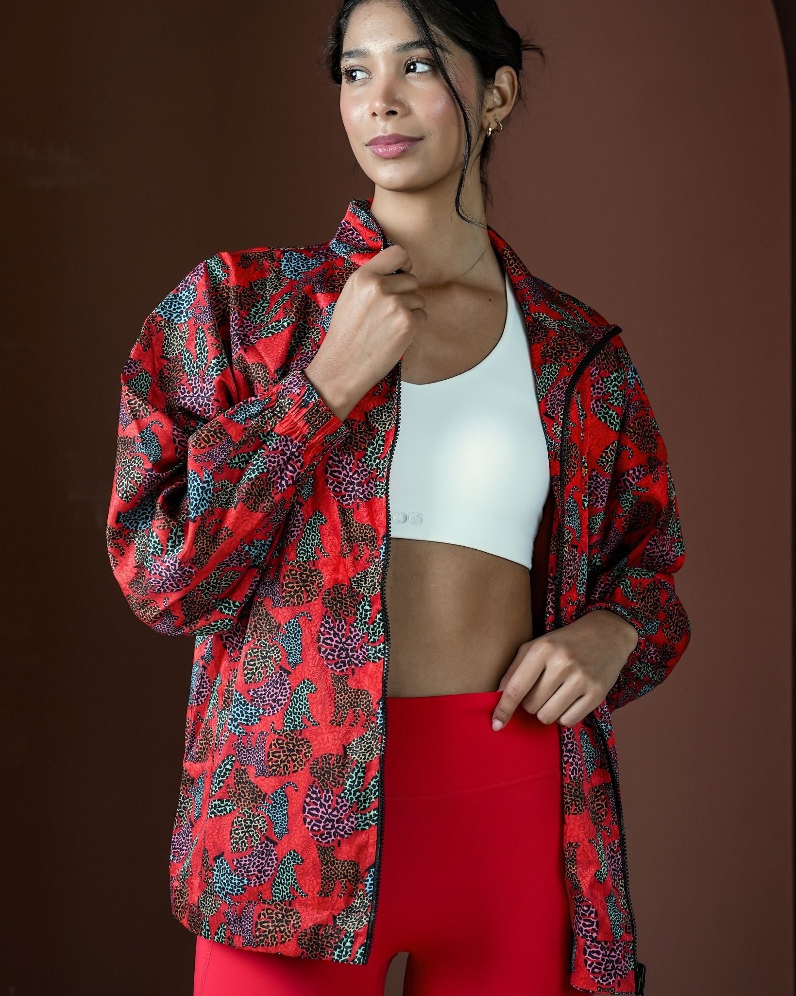 Woman wearing a red and black patterned jacket over a white sports bra and red leggings on a brown background