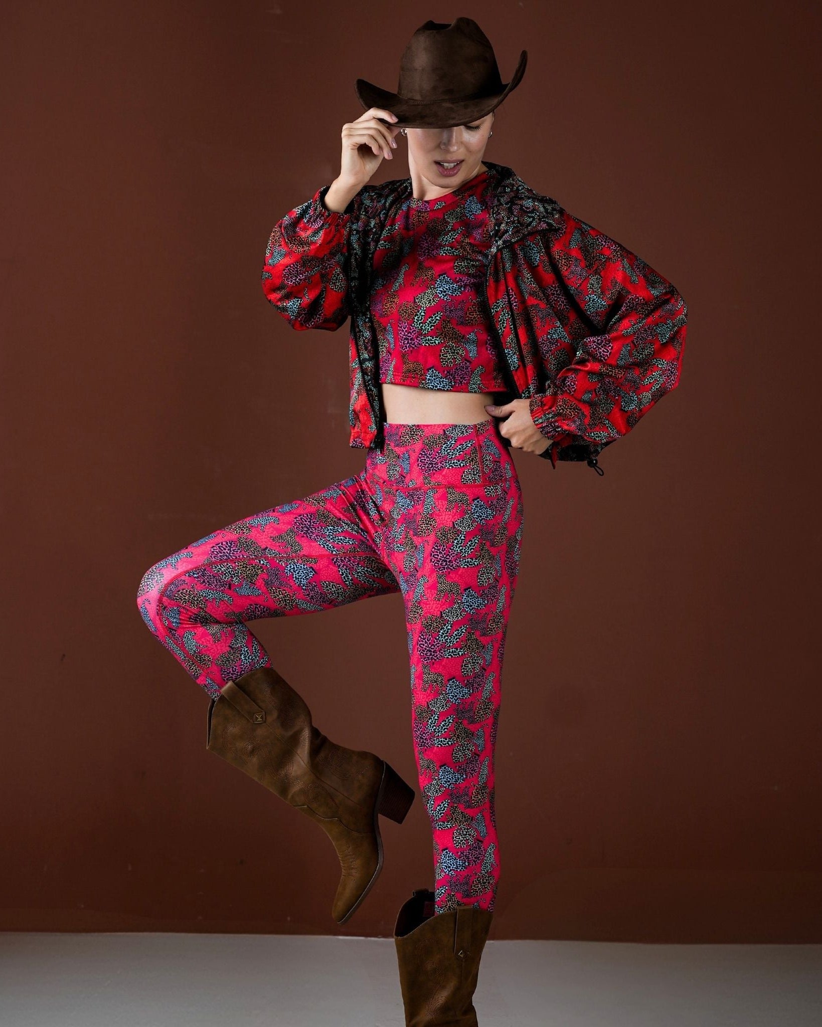 Person wearing a red and black patterned outfit with a cowboy hat on a brown background