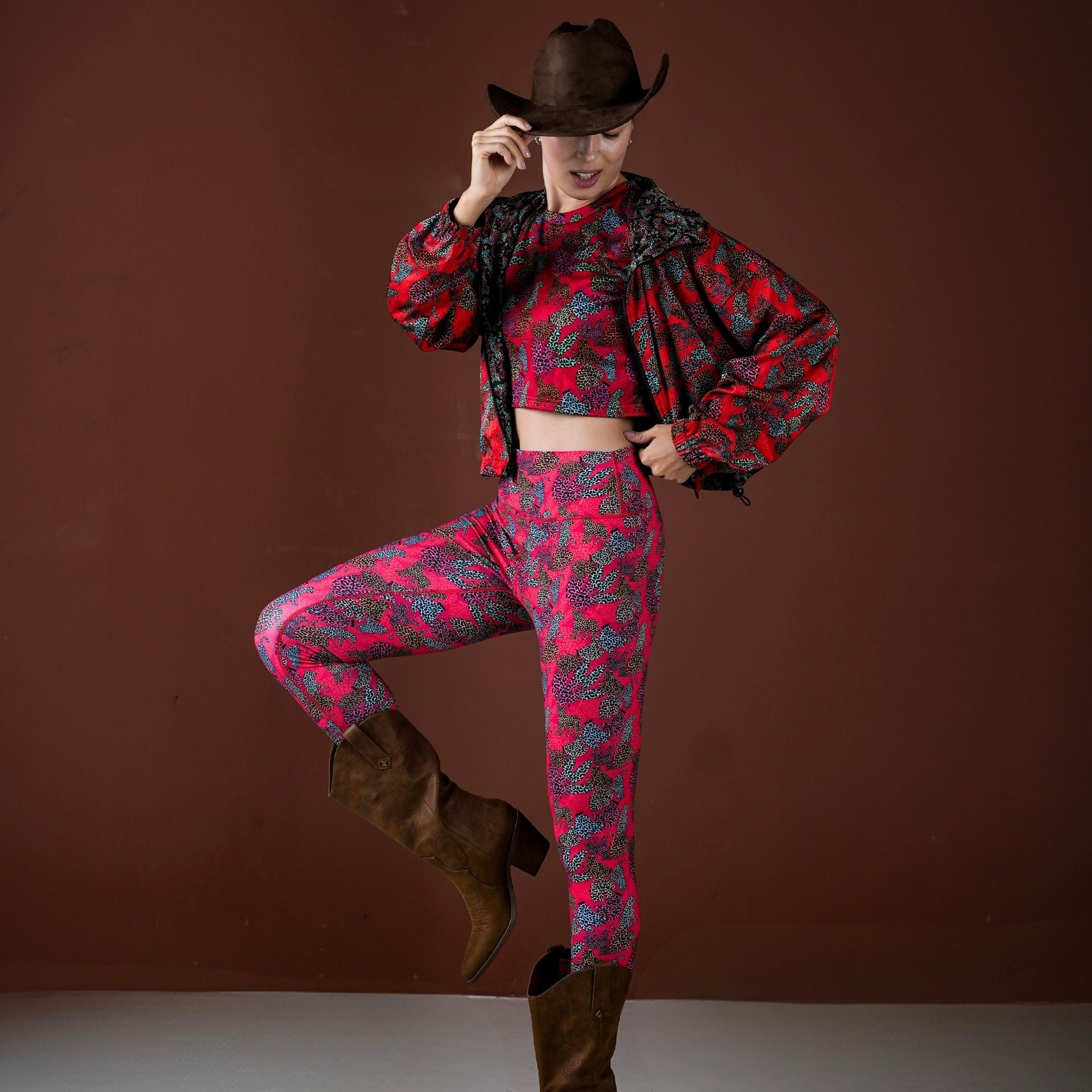 Person wearing a red and black patterned outfit with a cowboy hat on a brown background