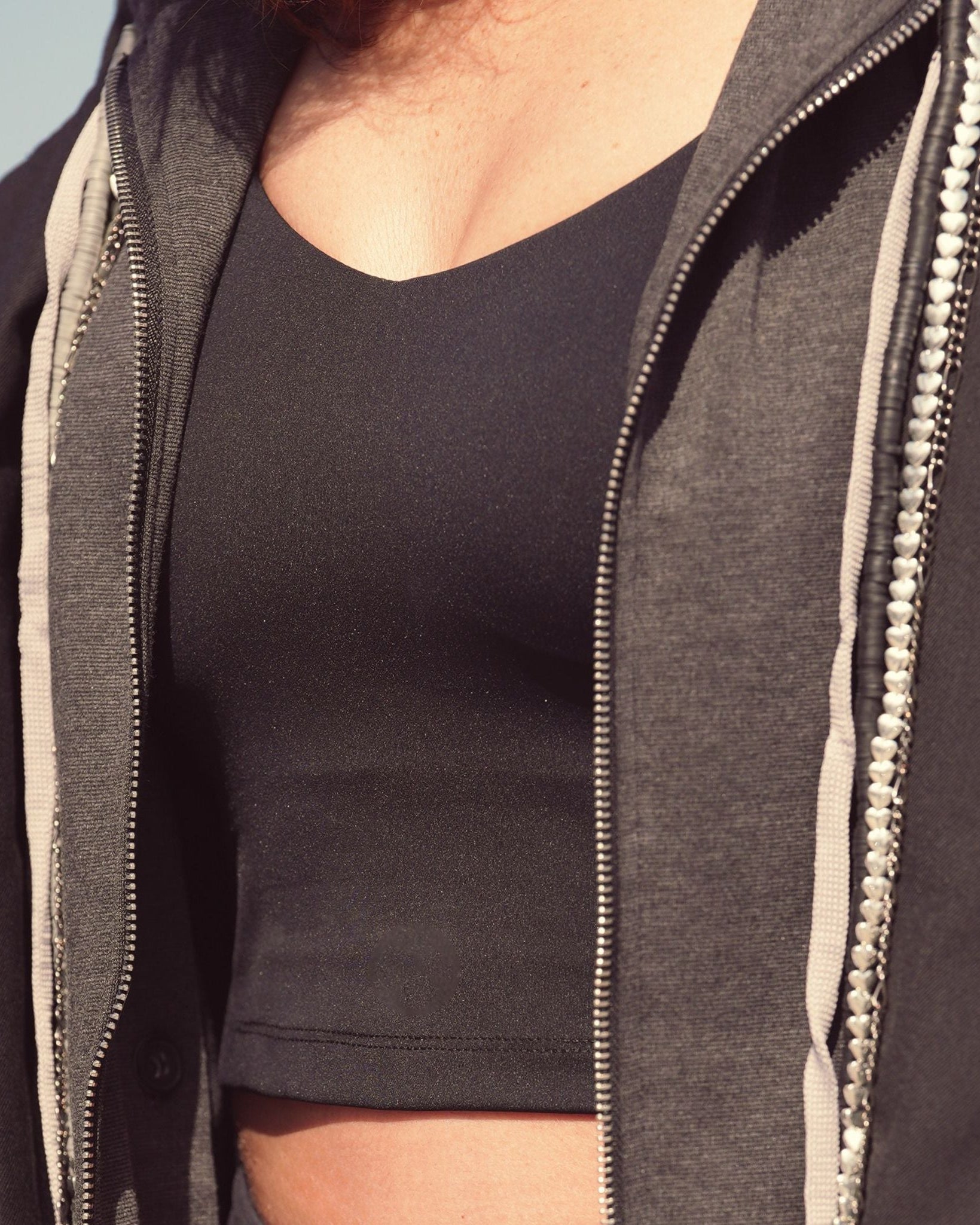 Person wearing a dark gray zip-up hoodie over a black shirt against a light blue sky.