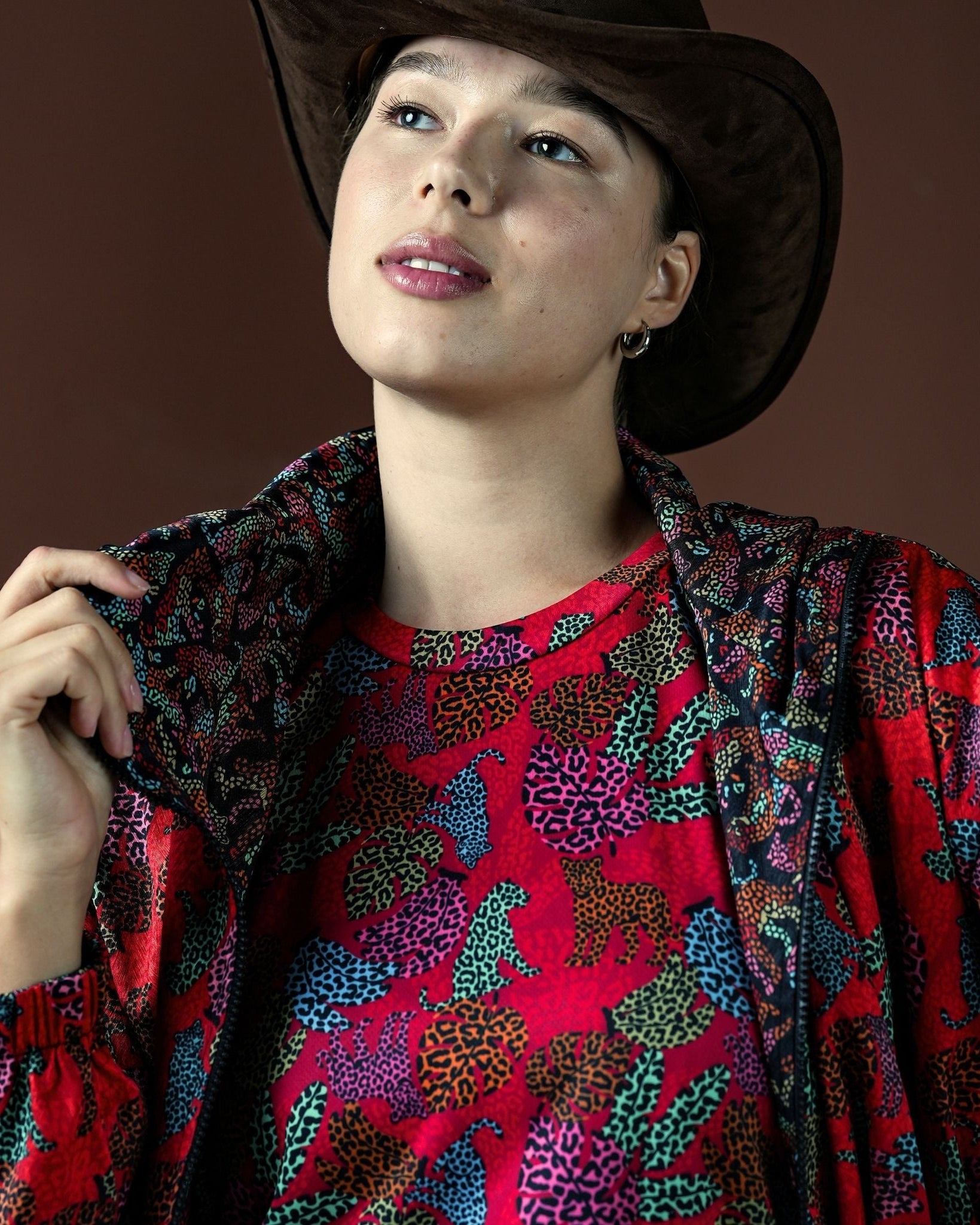 Woman wearing a colorful patterned jacket over a red shirt with a brown background