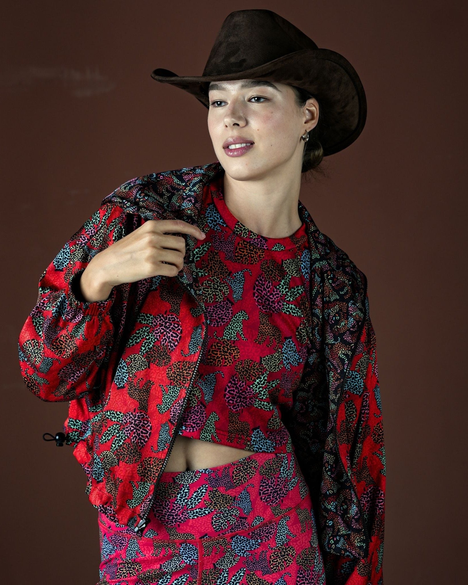 Woman wearing a red and black patterned outfit with a cowboy hat on a brown background