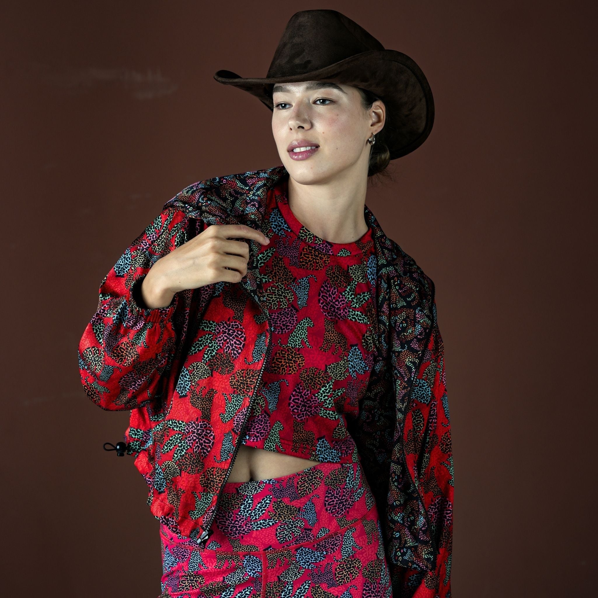 Woman wearing a red and black patterned outfit with a cowboy hat on a brown background