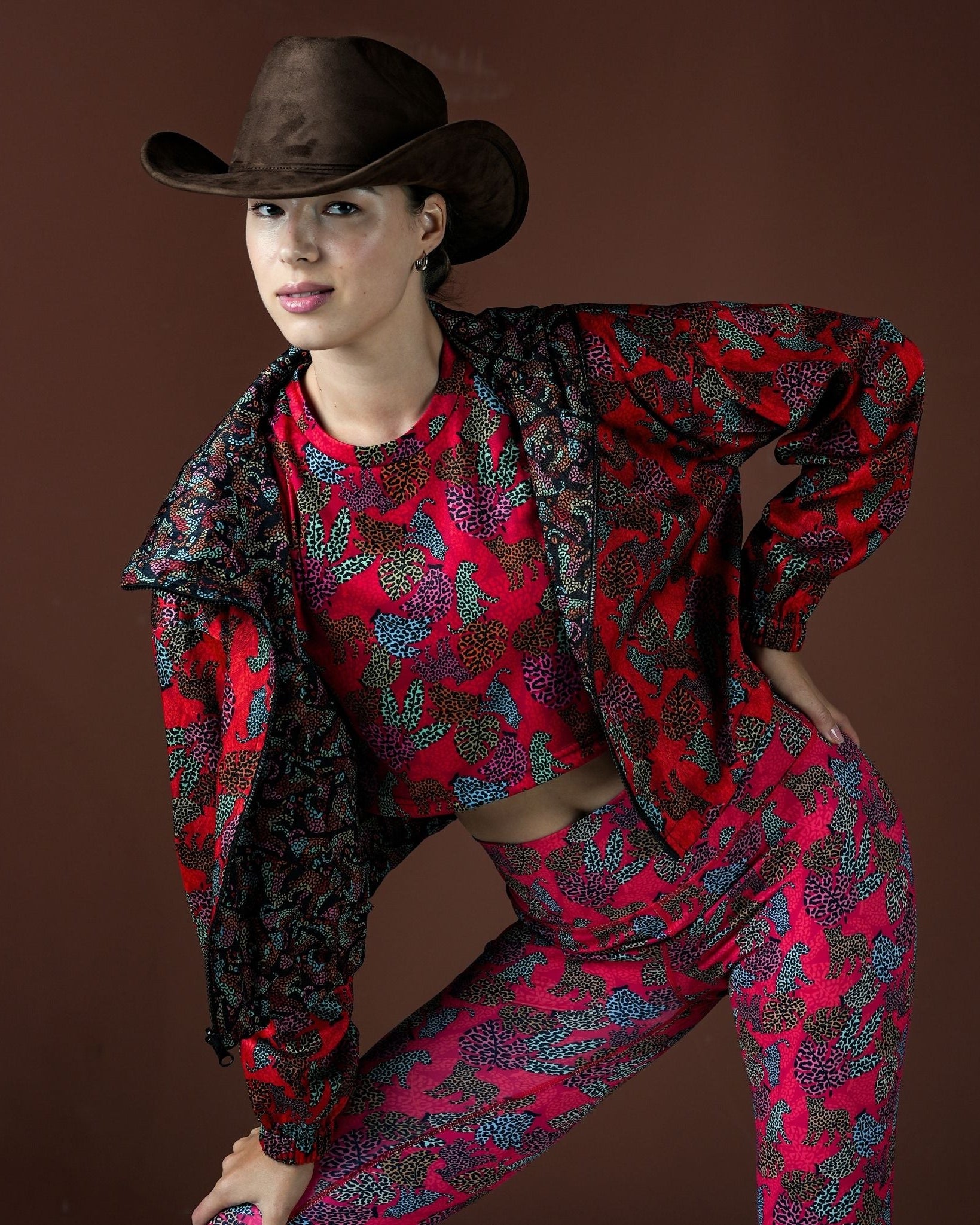 Person wearing a red and black patterned outfit with a cowboy hat on a brown background