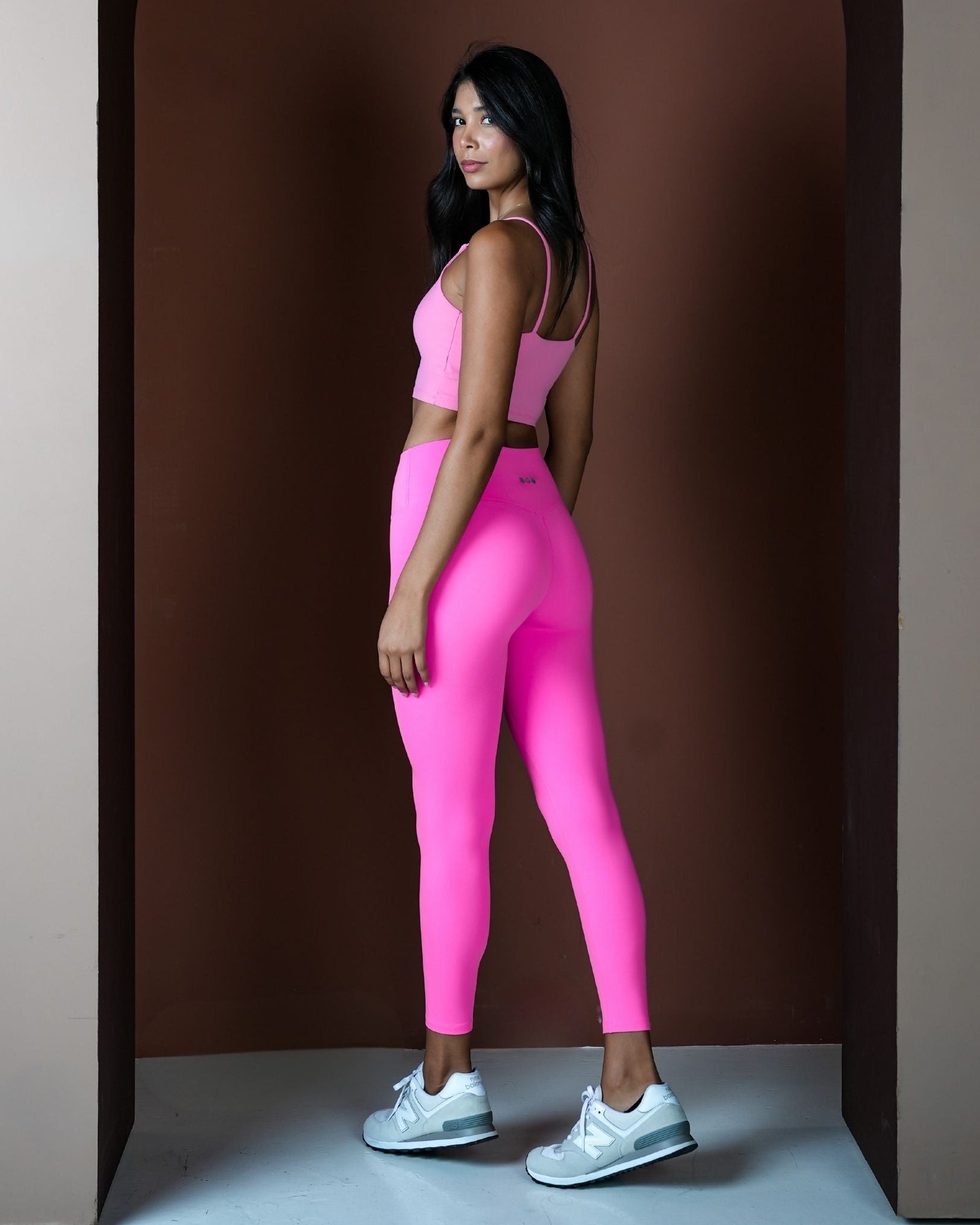Woman wearing a pink athletic outfit standing against a brown background