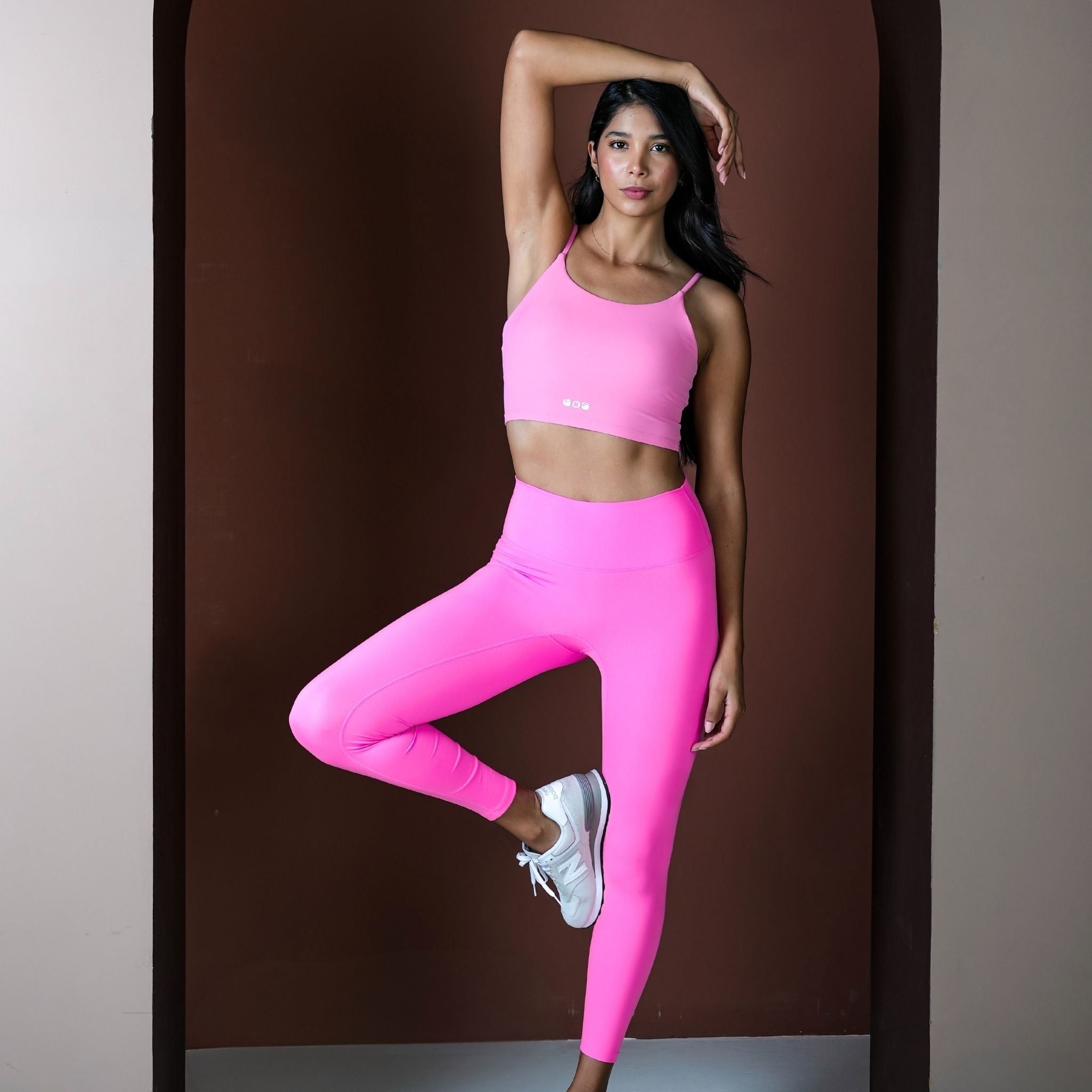 Woman in pink sports bra and leggings posing against a brown background