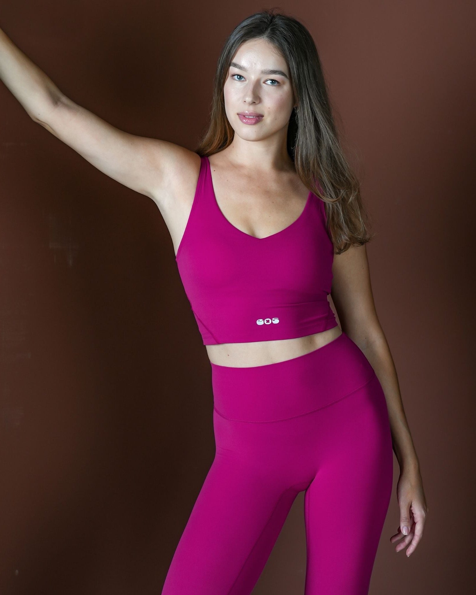 Woman wearing a bright pink sports bra and leggings against a brown background