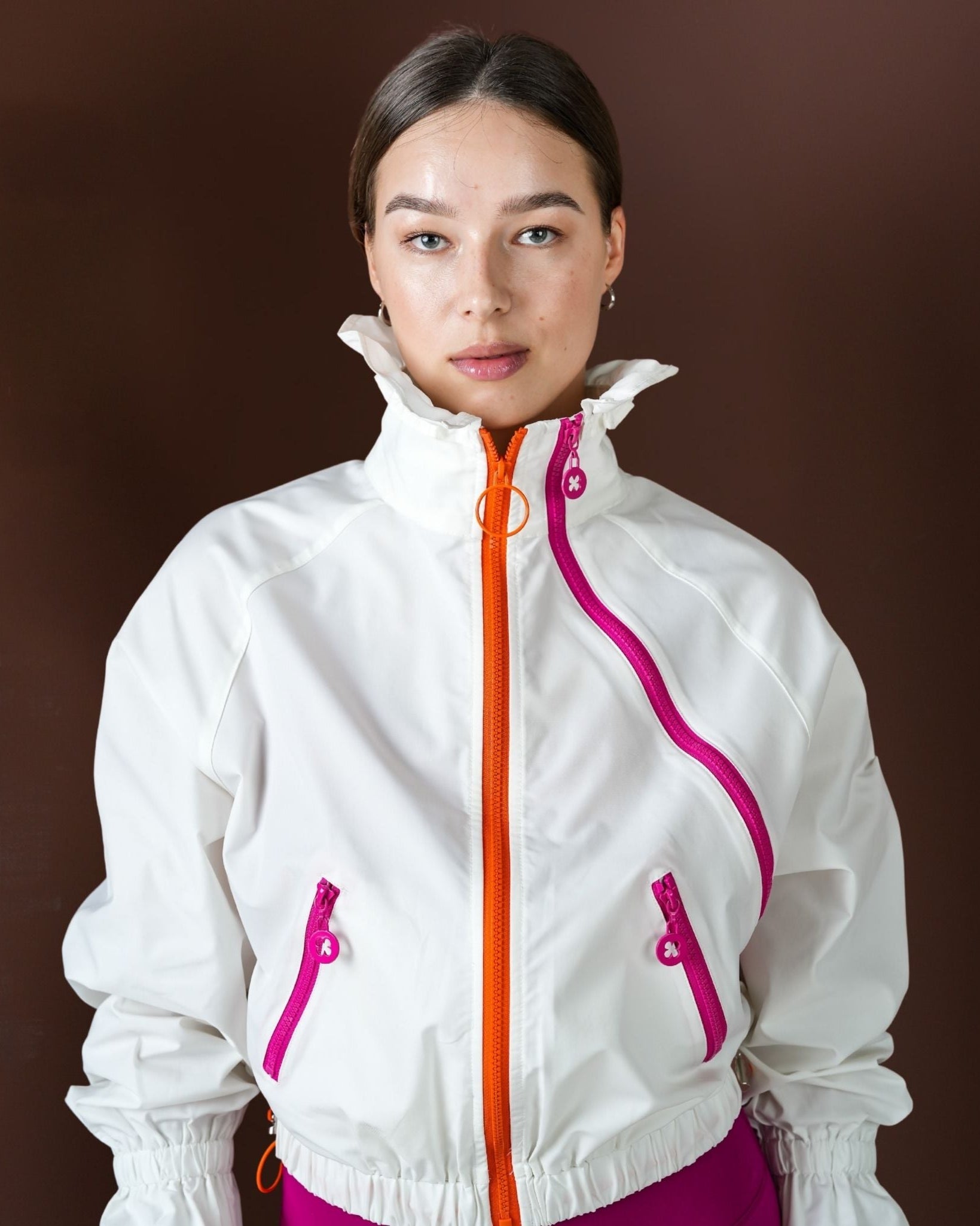 Person wearing a white jacket with pink accents on a brown background