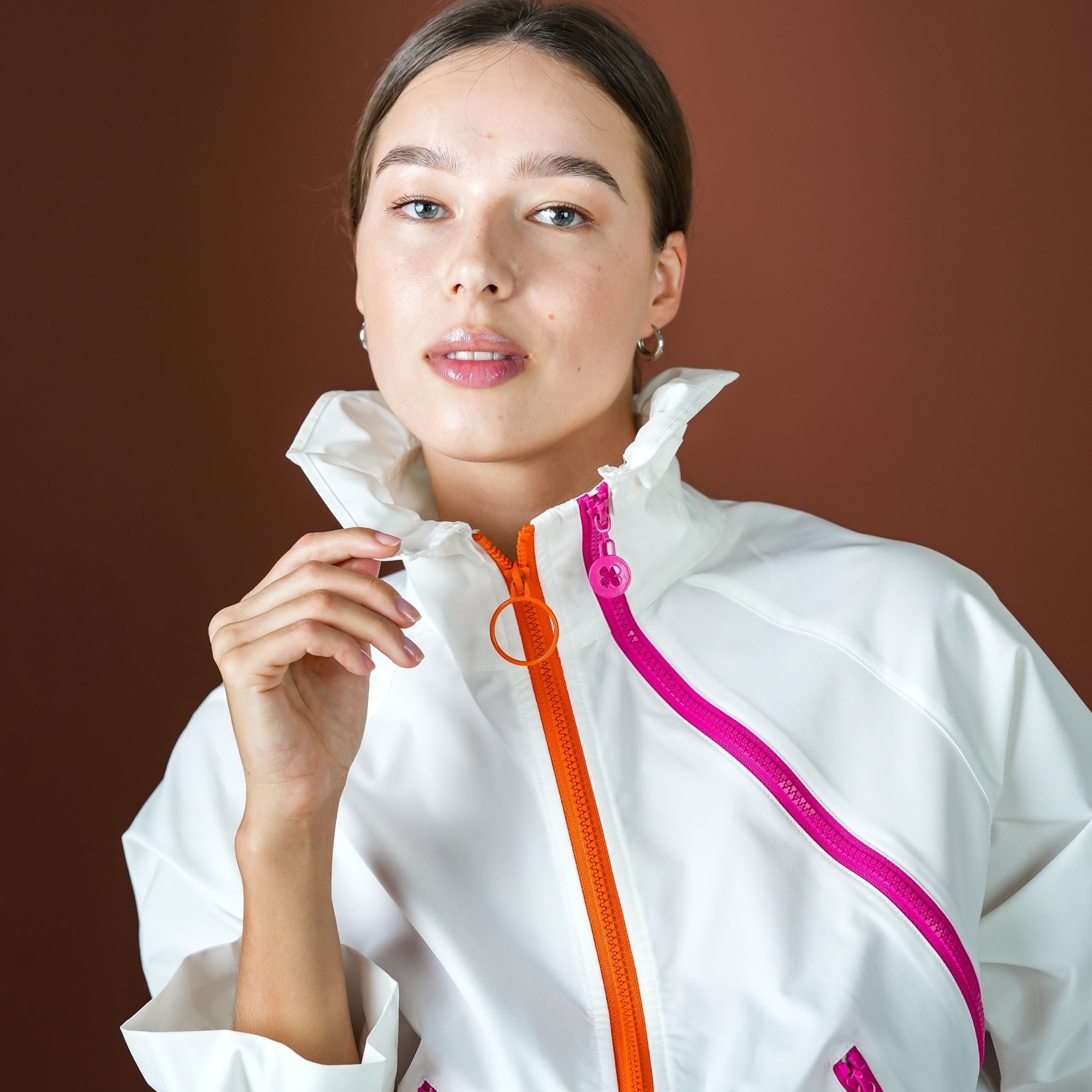 Woman wearing a white jacket with colorful zippers on a brown background