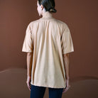 Person wearing a beige t-shirt against a brown background