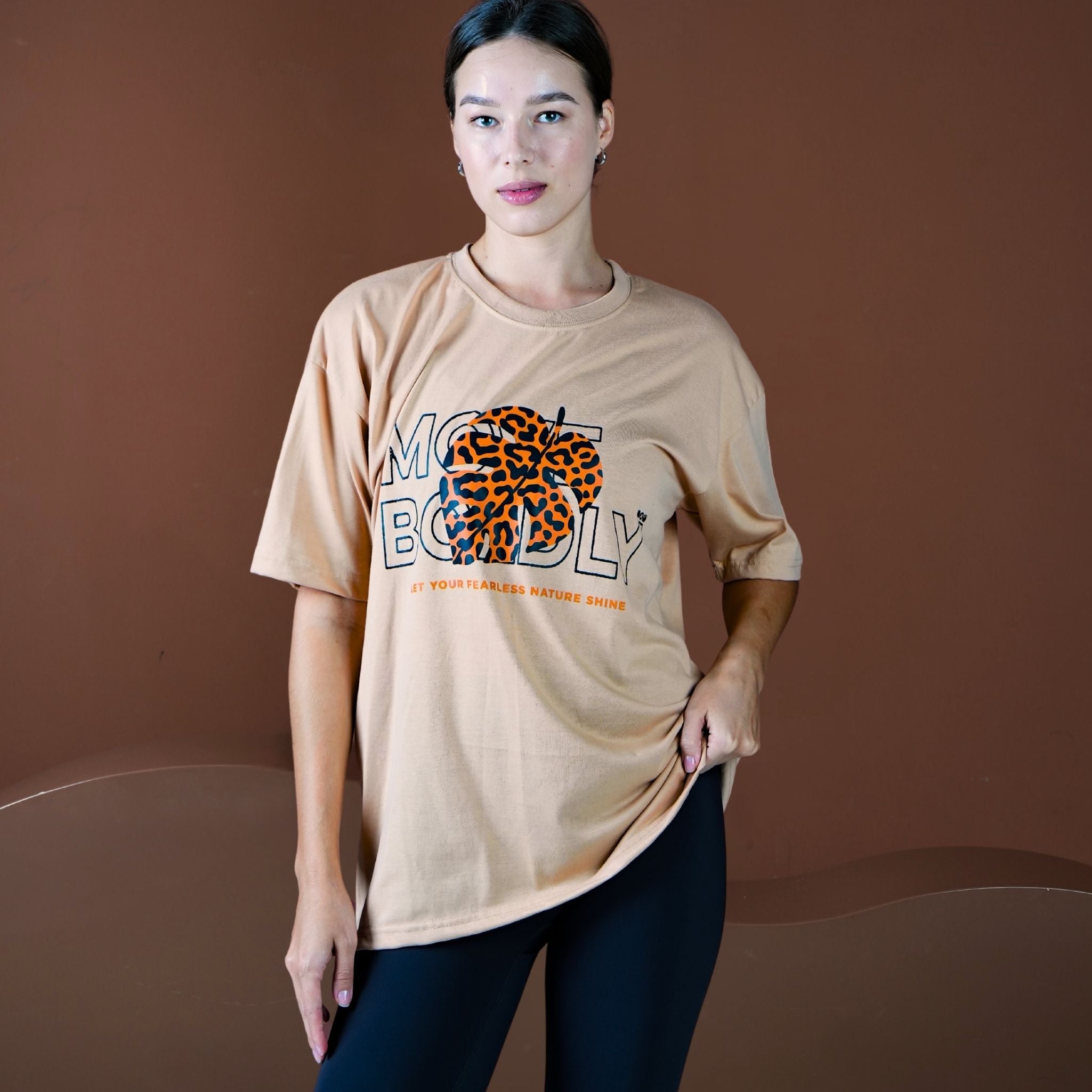 Woman wearing a beige t-shirt with a graphic design on a brown background