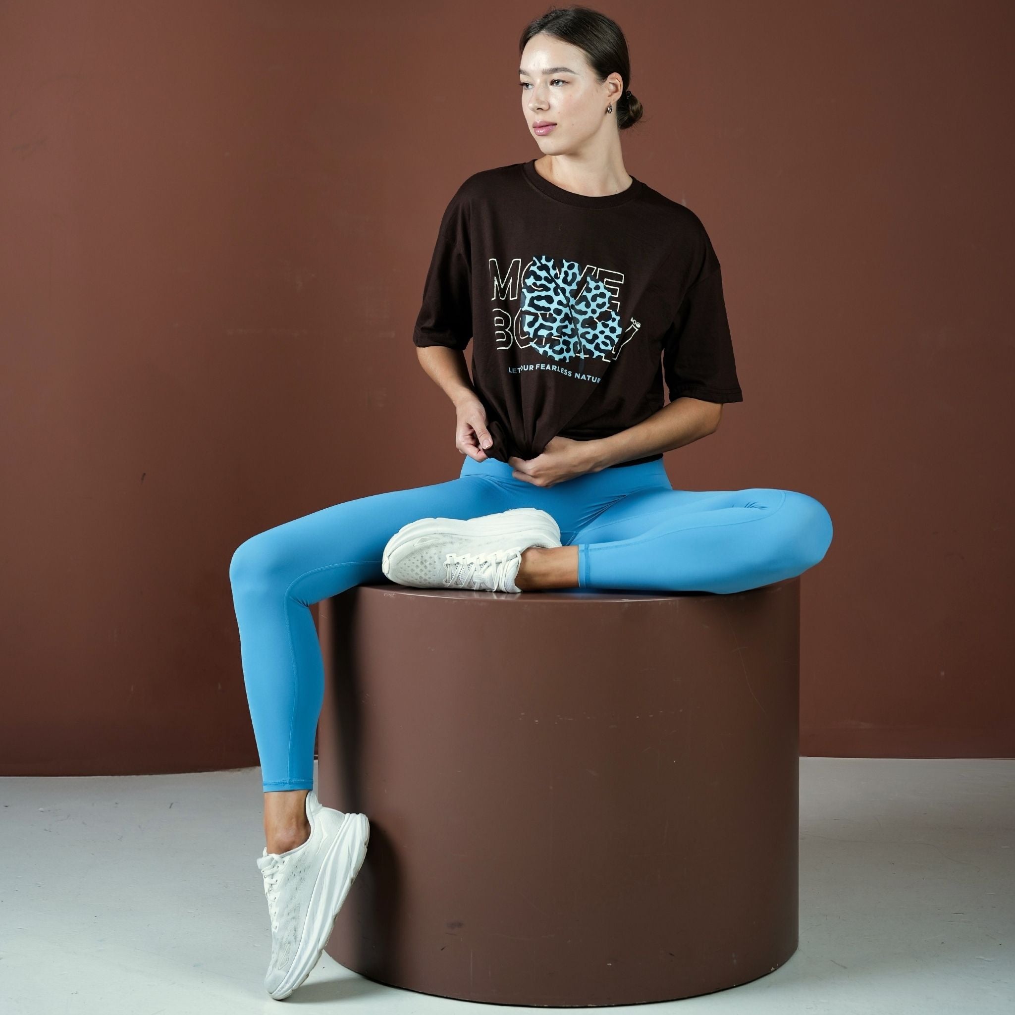 Person sitting on a brown cylindrical stool against a brown background