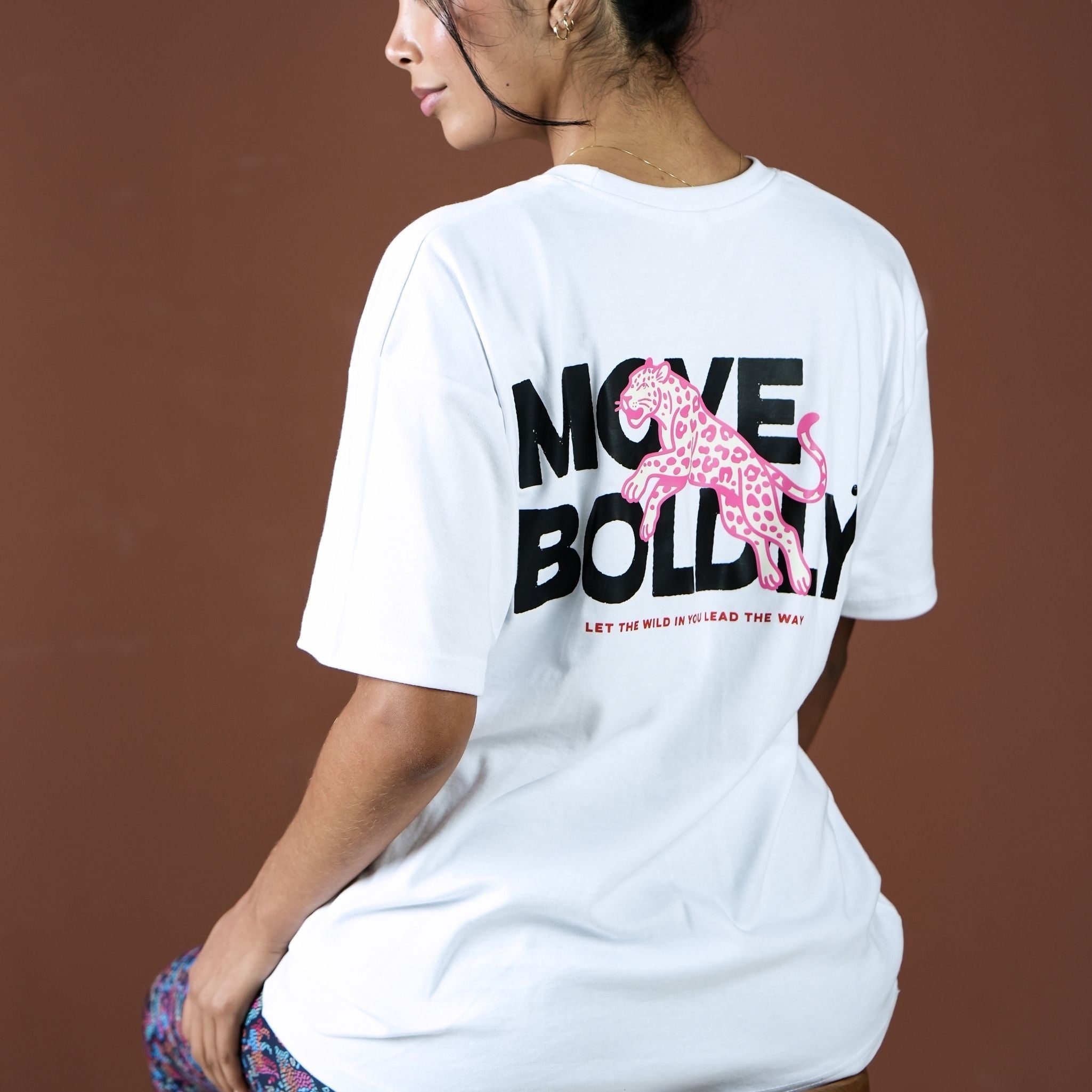 Person wearing a white t-shirt with a pink panther graphic and text on the back against a brown background