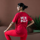 Person wearing a red 'MOVE BODY' t-shirt sitting on a couch with a plant in the background.