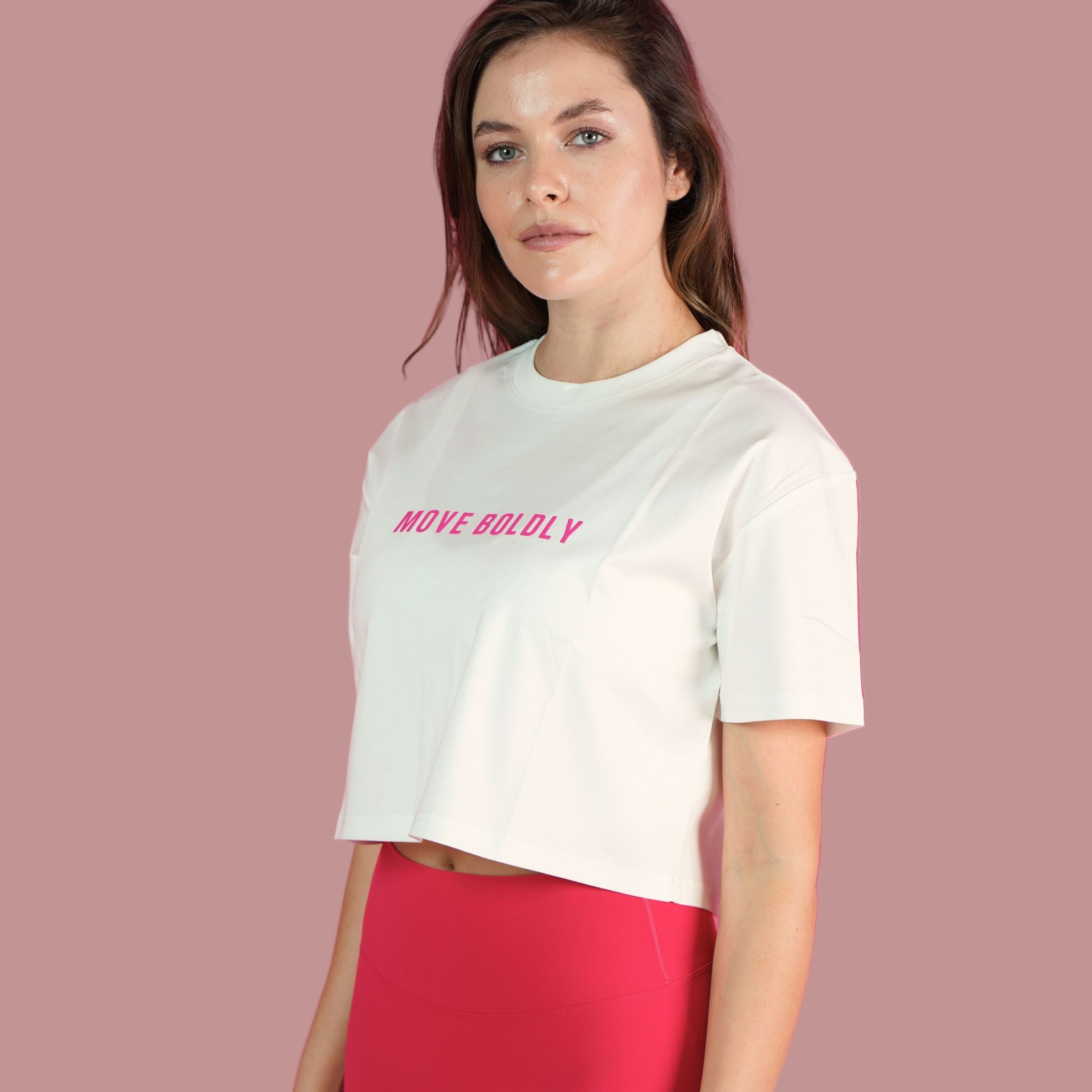 Woman wearing a white t-shirt with 'MOVE BOLDLY' text on a pink background