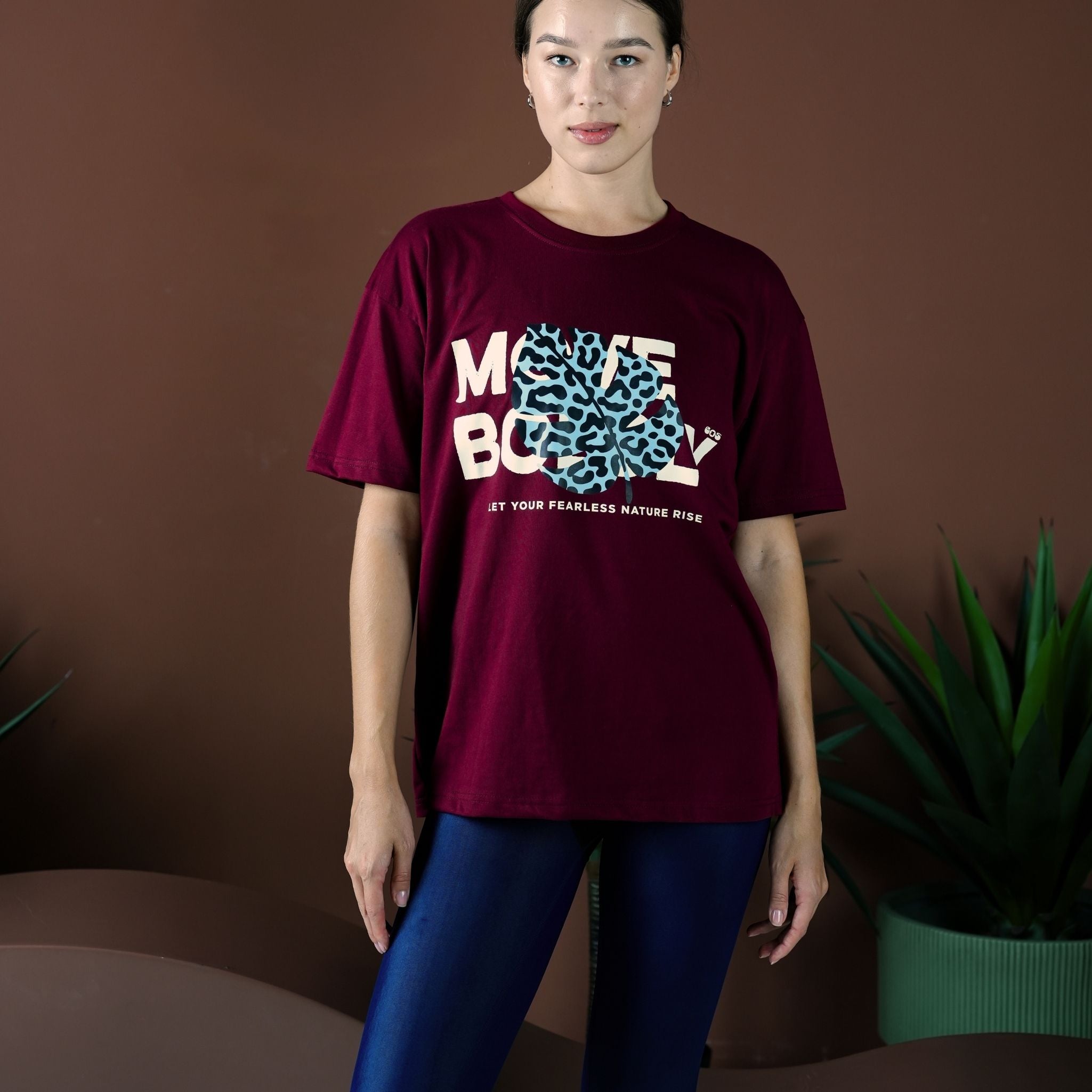 Person wearing a burgundy t-shirt with a graphic design on a brown background