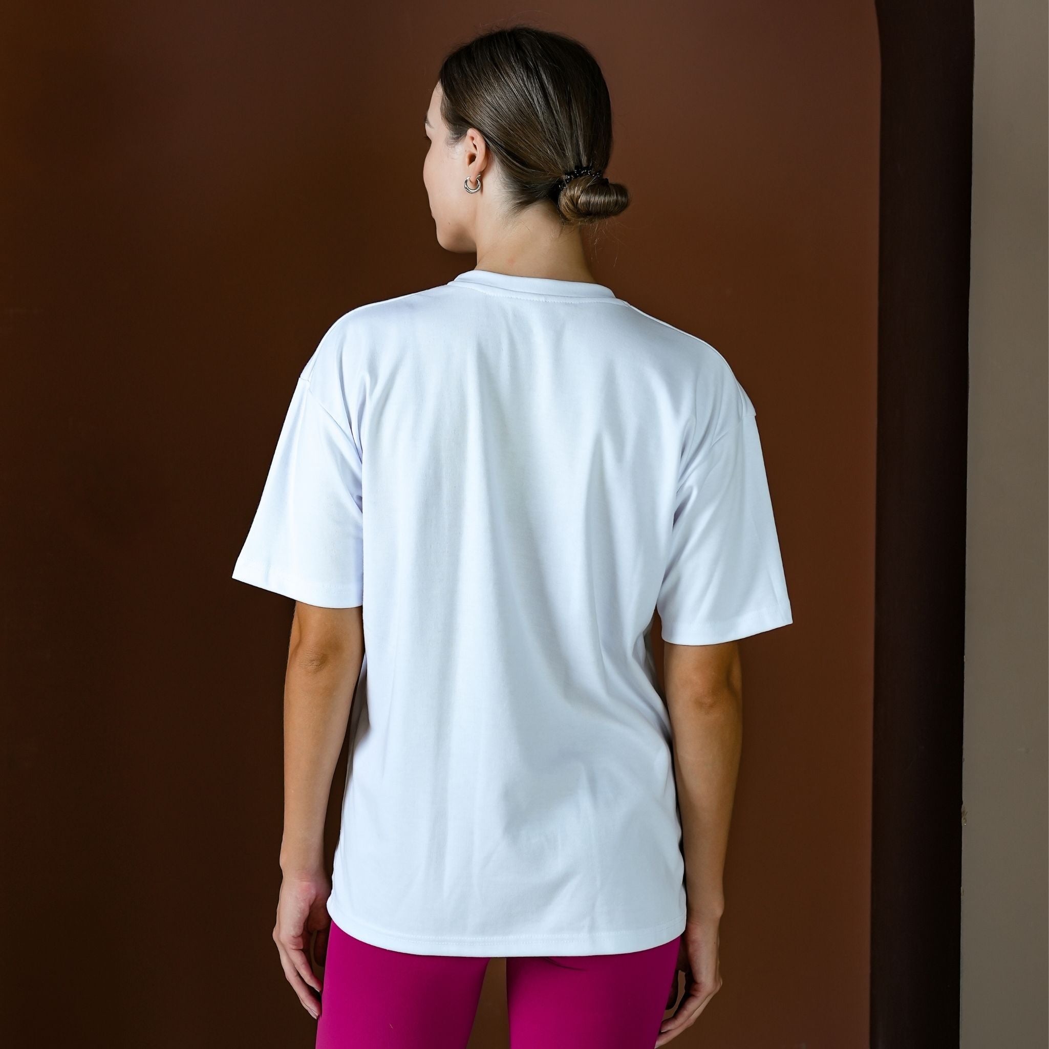 Person wearing a white t-shirt and pink pants against a brown background