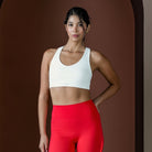 Woman wearing a white sports bra and red leggings against a brown background