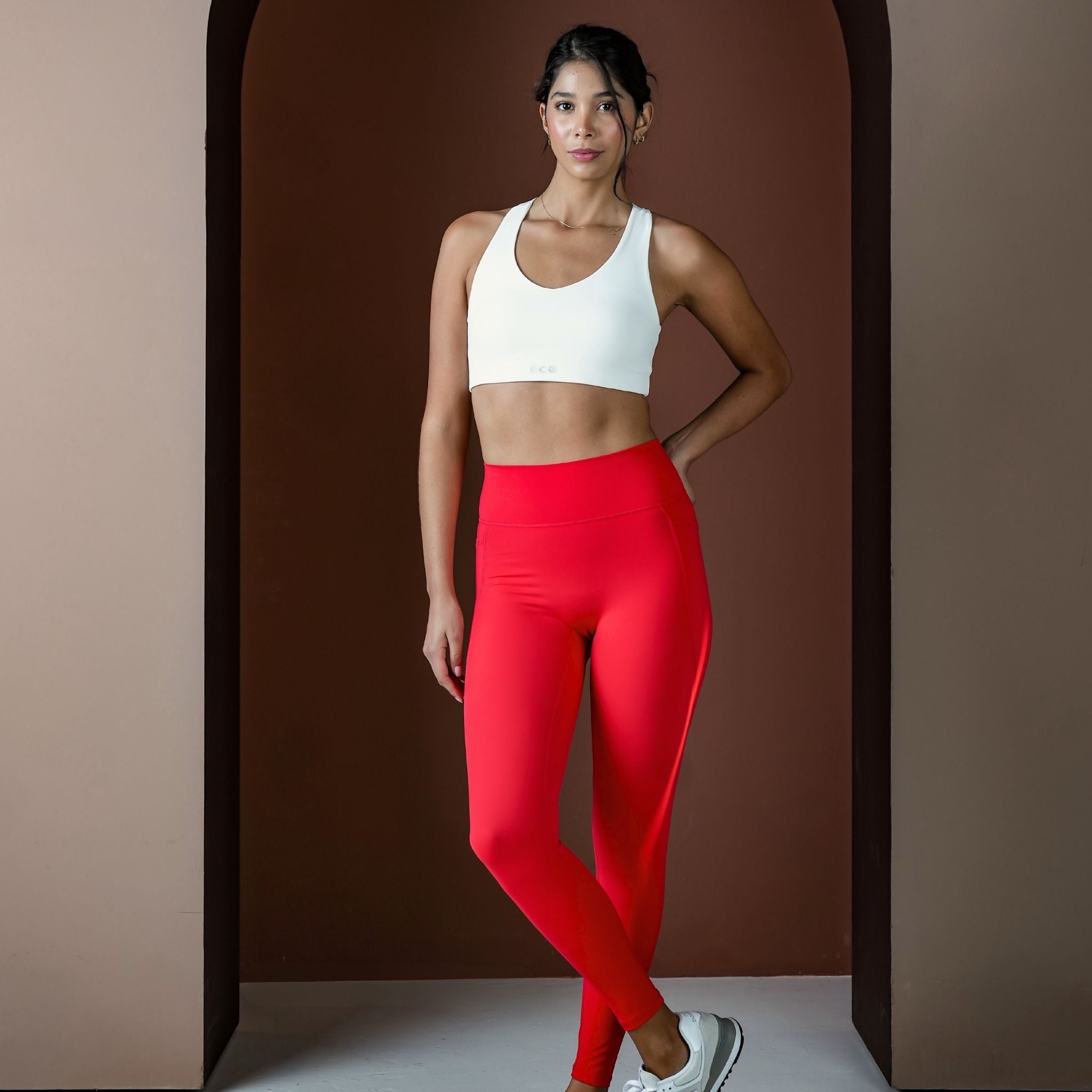 Woman wearing a white sports bra and red leggings against a brown background