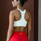 Woman wearing a white sports bra and red leggings against a brown background