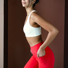 Woman wearing a white sports bra and red leggings against a brown background