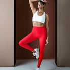Woman in red leggings and white sports bra posing against a brown background