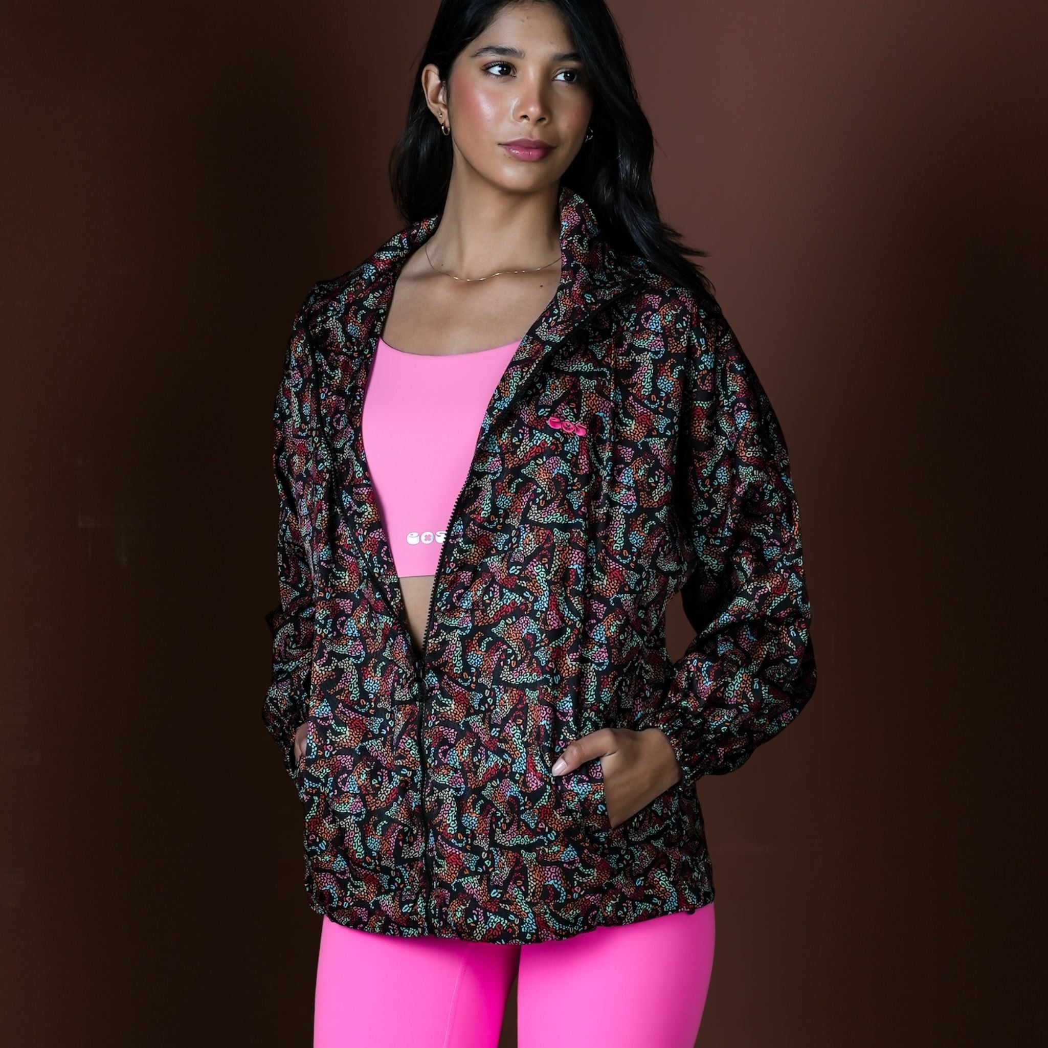Woman wearing a patterned jacket over a pink top and leggings on a brown background