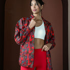 Woman wearing a red and black patterned jacket over a white sports bra and red leggings on a brown background