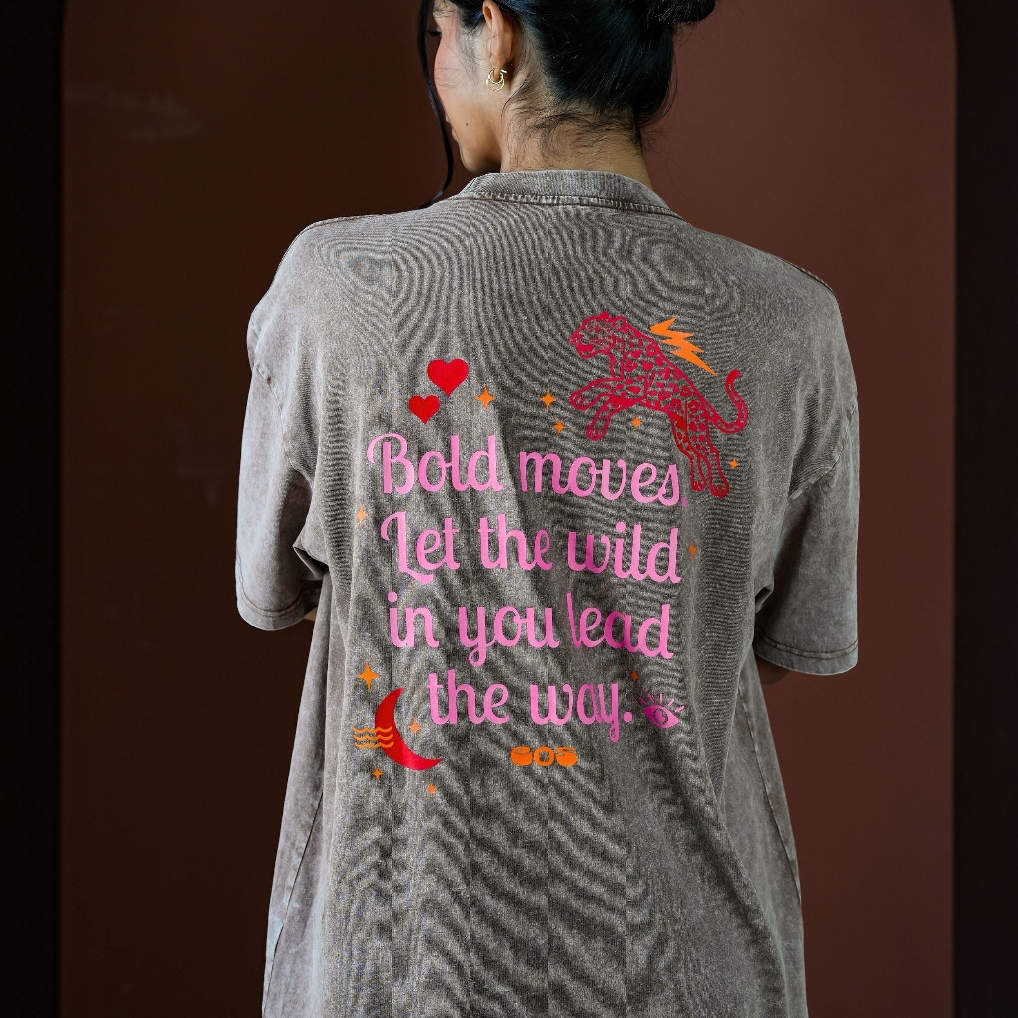 Person wearing a gray t-shirt with a motivational quote and graphic on the back against a brown background
