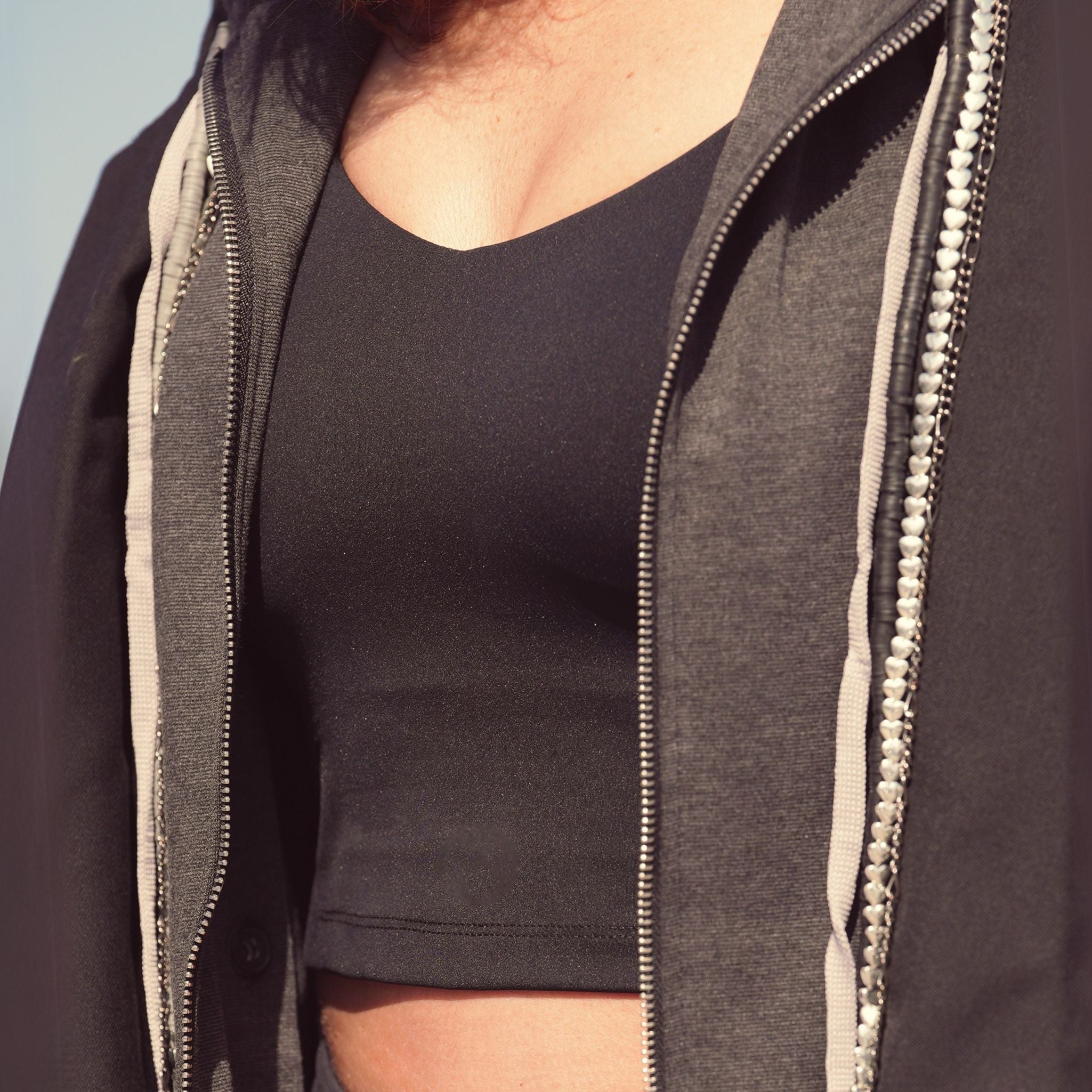 Person wearing a dark gray zip-up hoodie over a black shirt against a light blue sky.