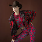 Person wearing a red and black patterned outfit with a cowboy hat on a brown background