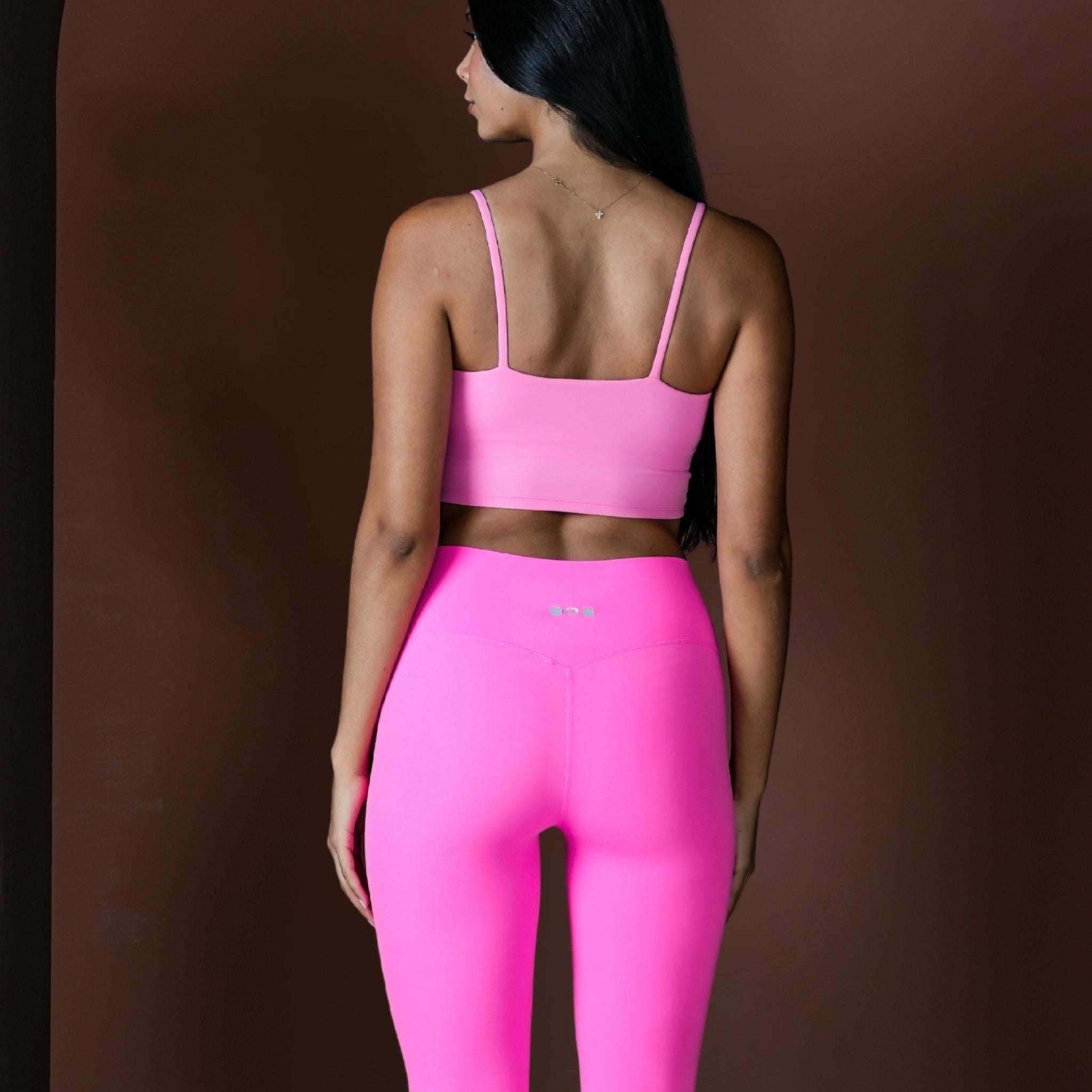 Person wearing a pink sports bra and leggings on a brown background