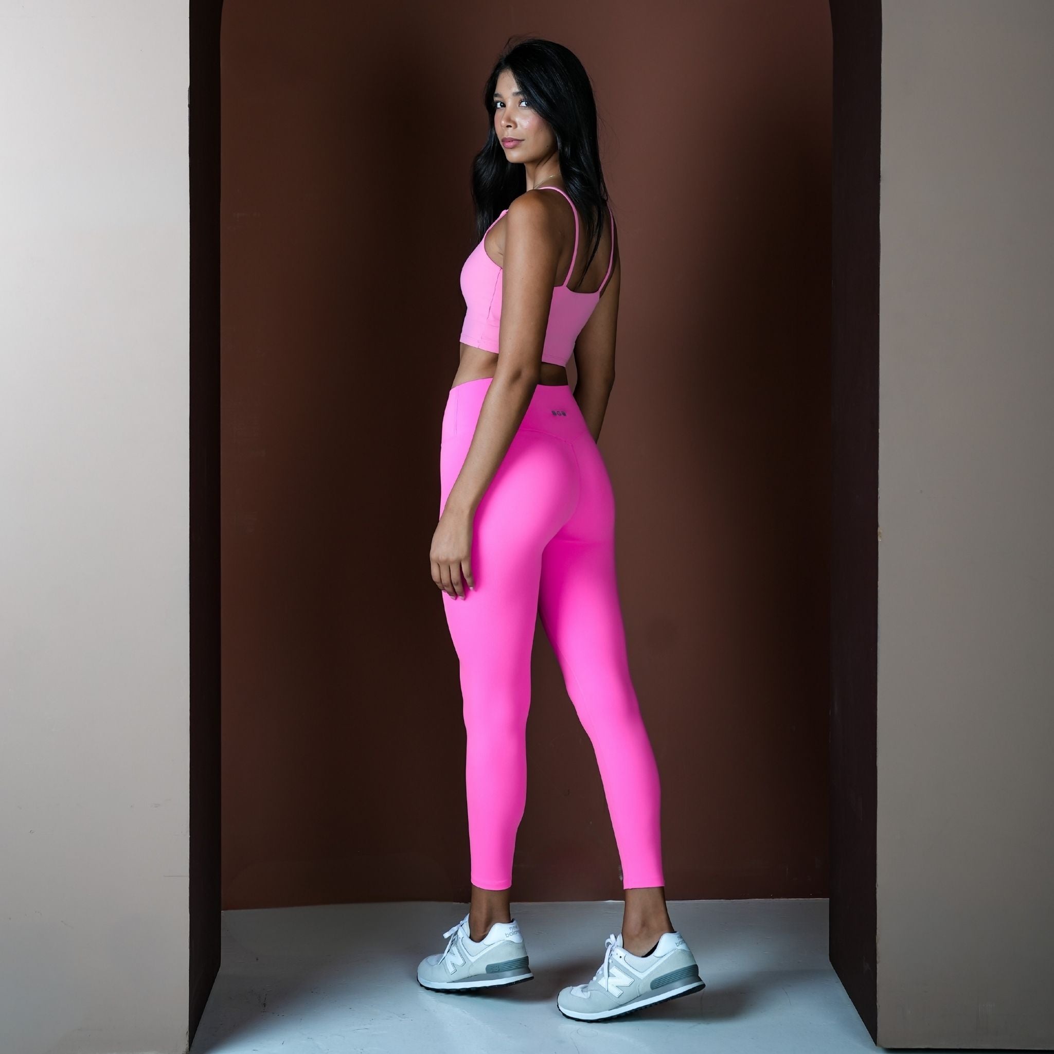 Woman wearing a pink athletic outfit standing against a brown background