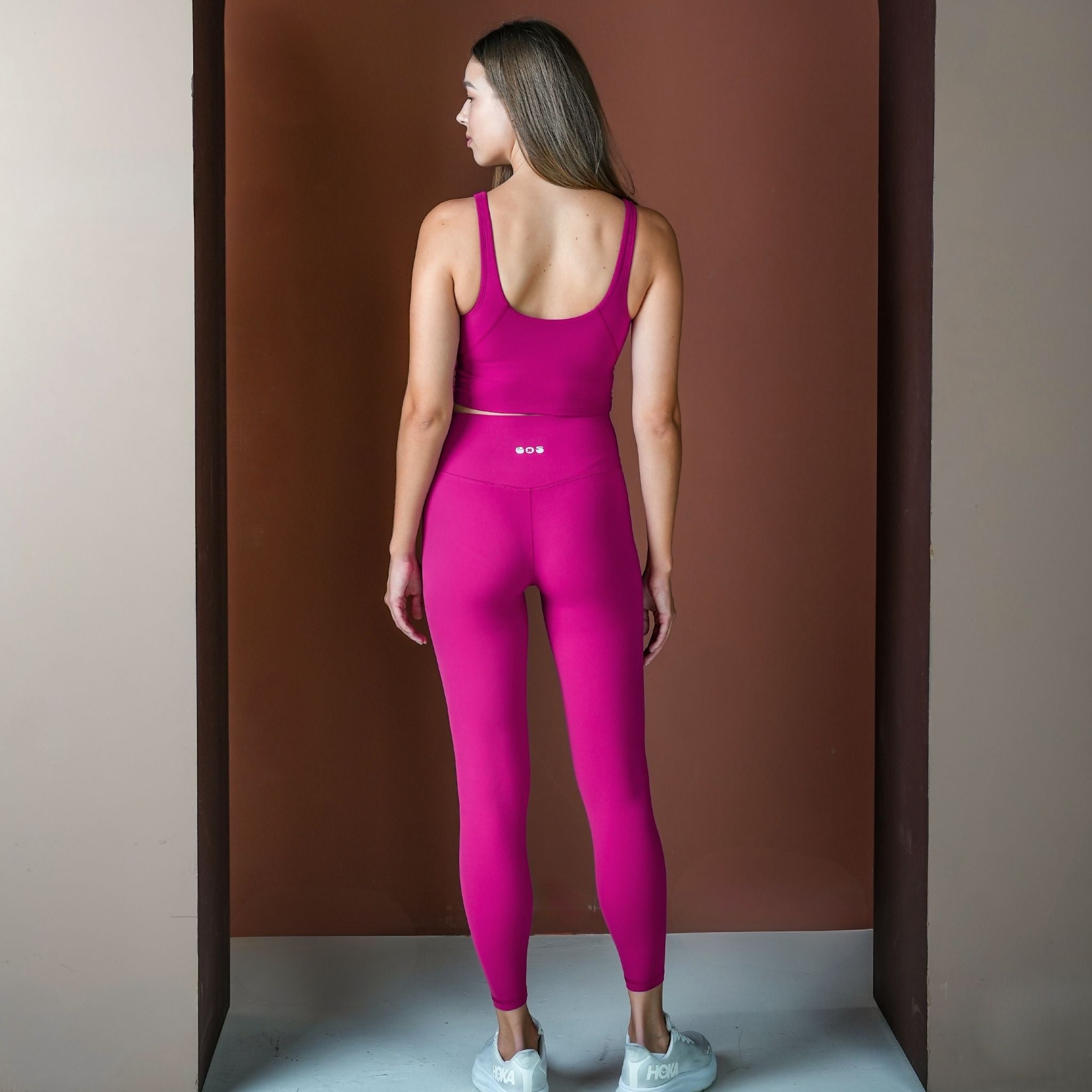 Woman wearing a pink athletic outfit standing against a brown wall.
